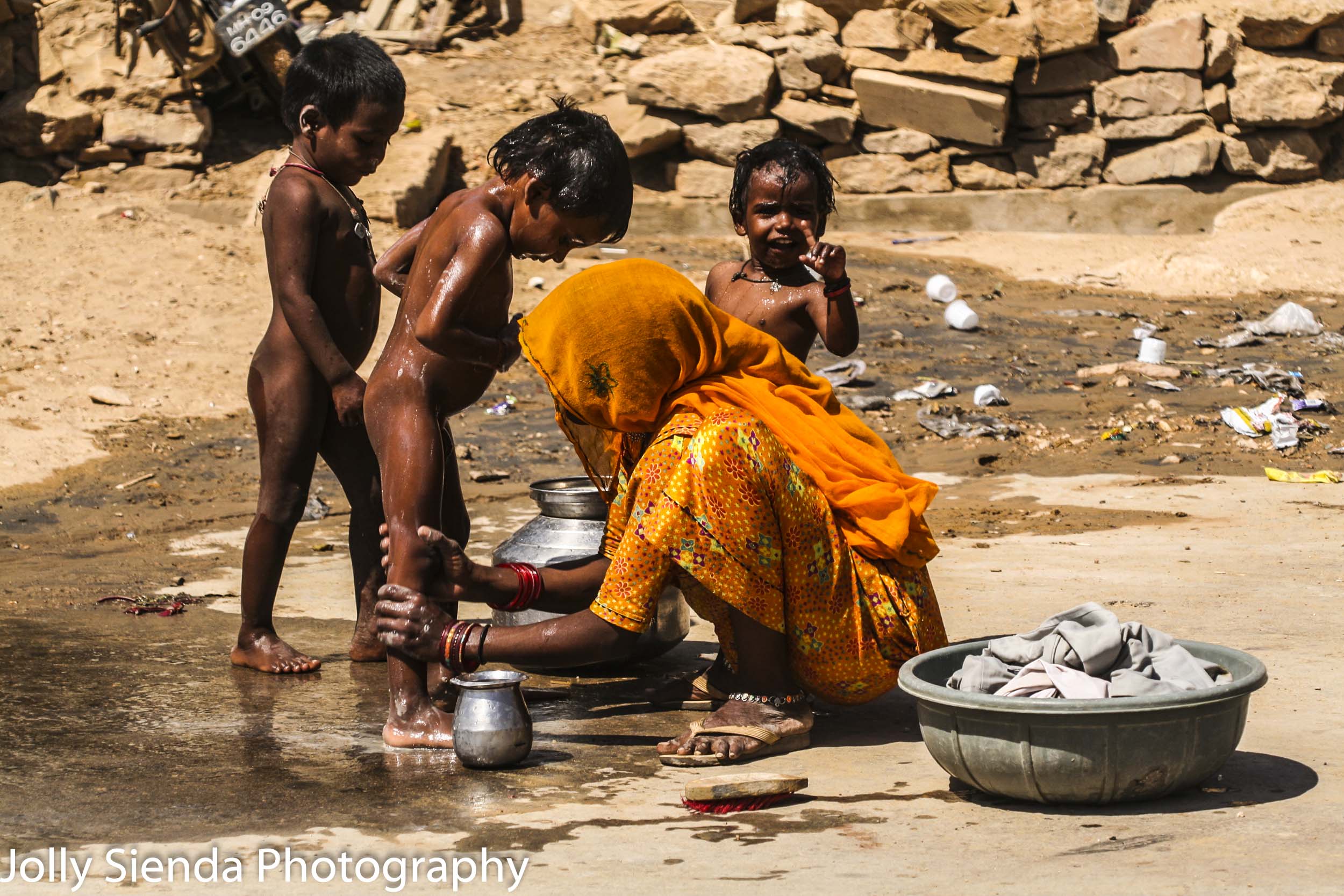 Mother bathes her children on the dirt street 