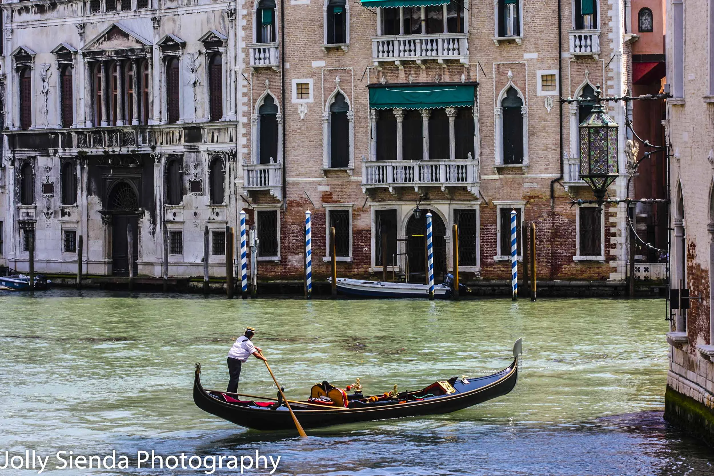 Gondolier steers his shiny, black gondola through a canal near V