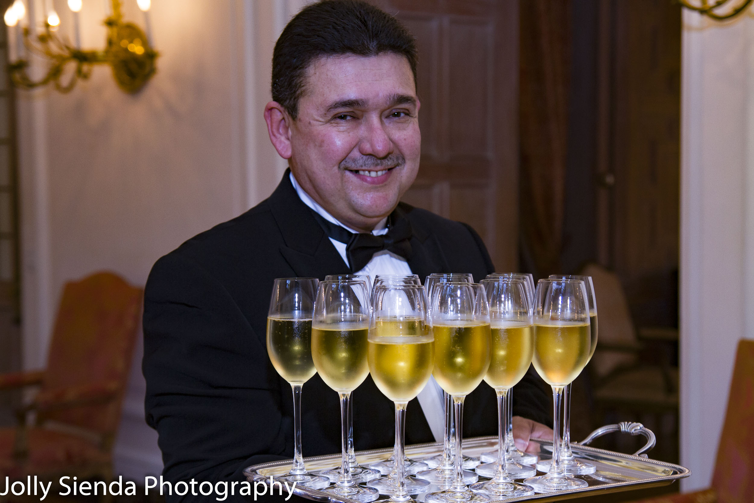 Smiling waiter carries wine glasses, French Ambassadors Dinner