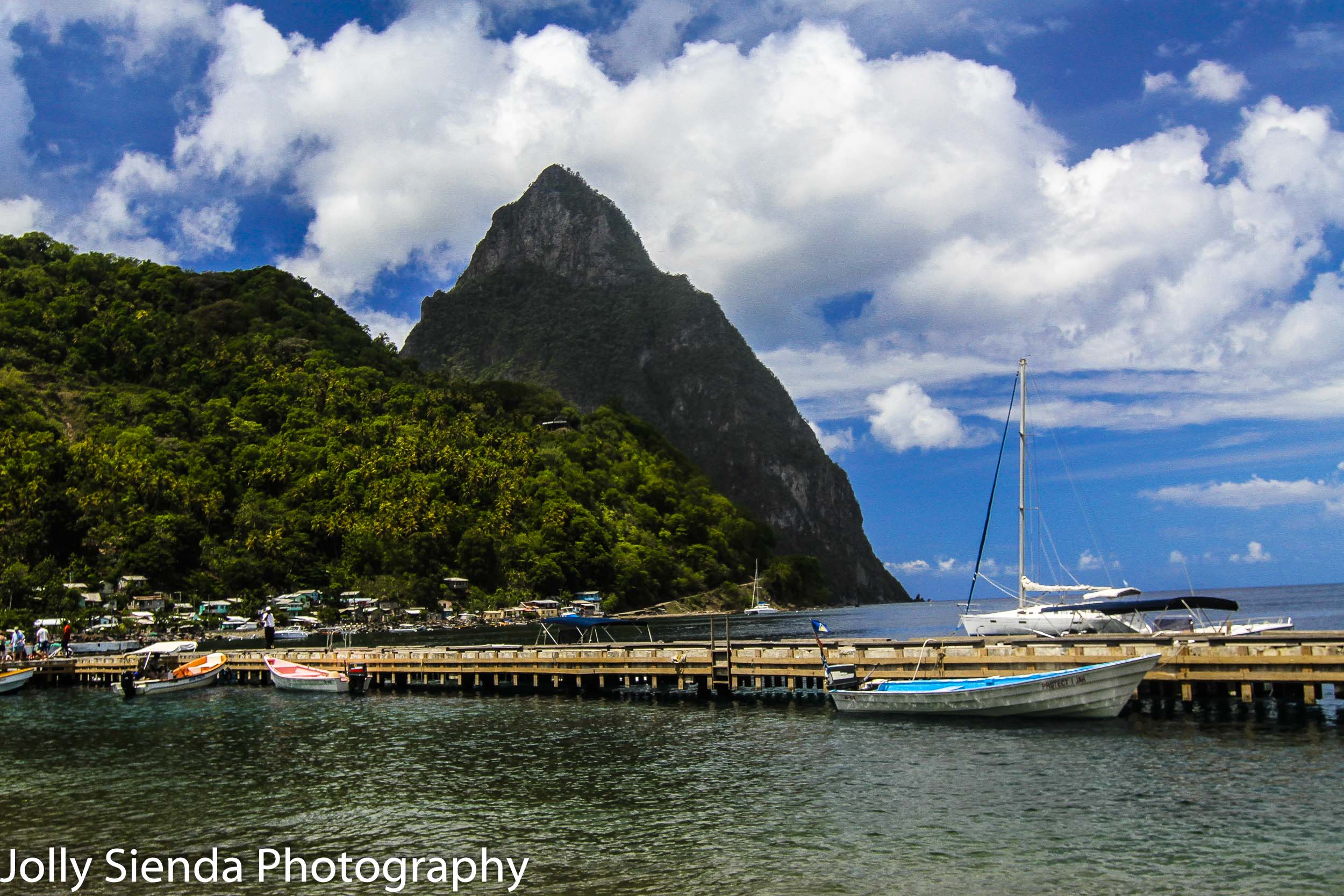 The long dock with colored boats with the Pitons and a village i