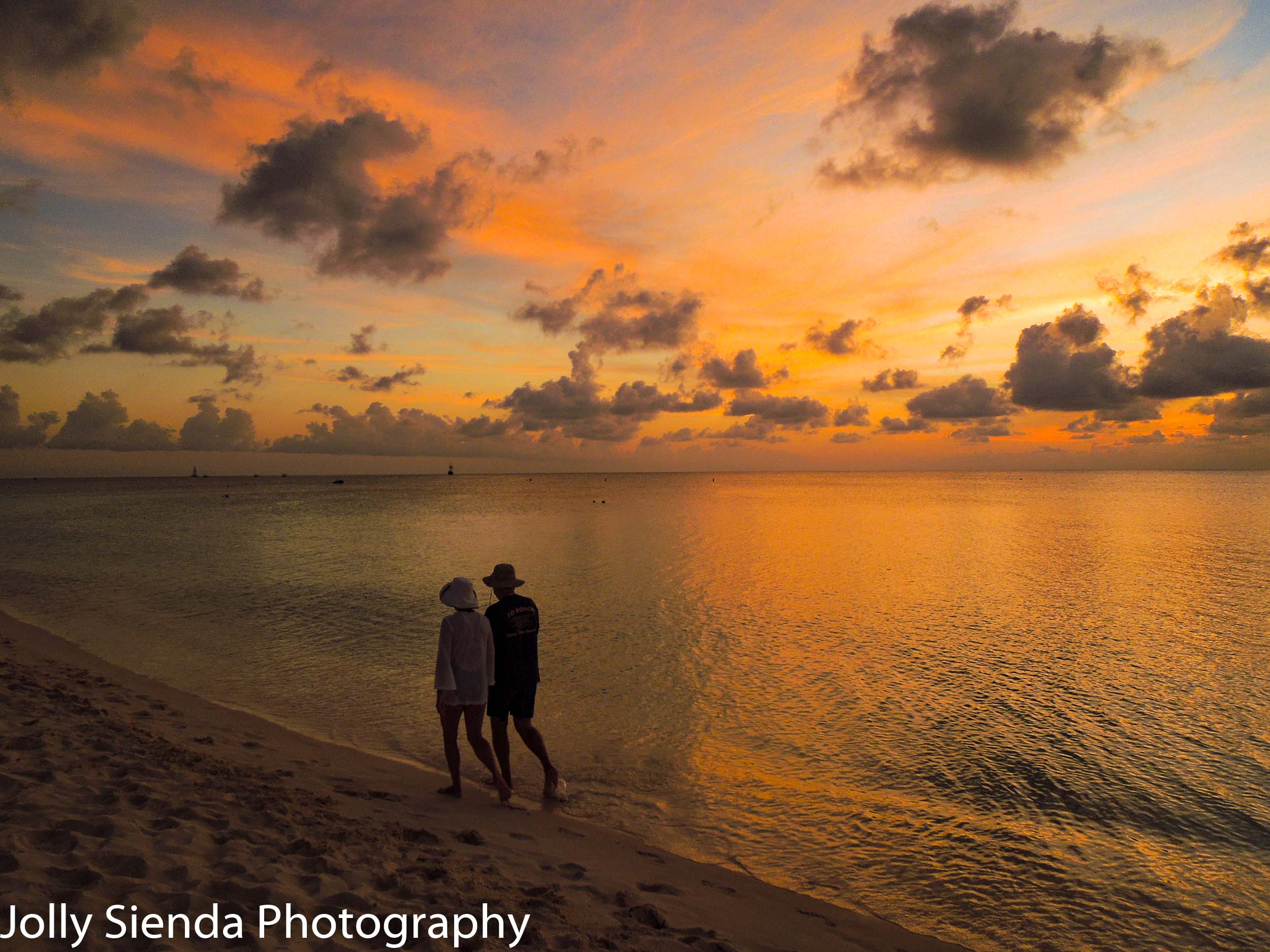 A couple walking on Seven Mile Beach during a golden, pink, suns