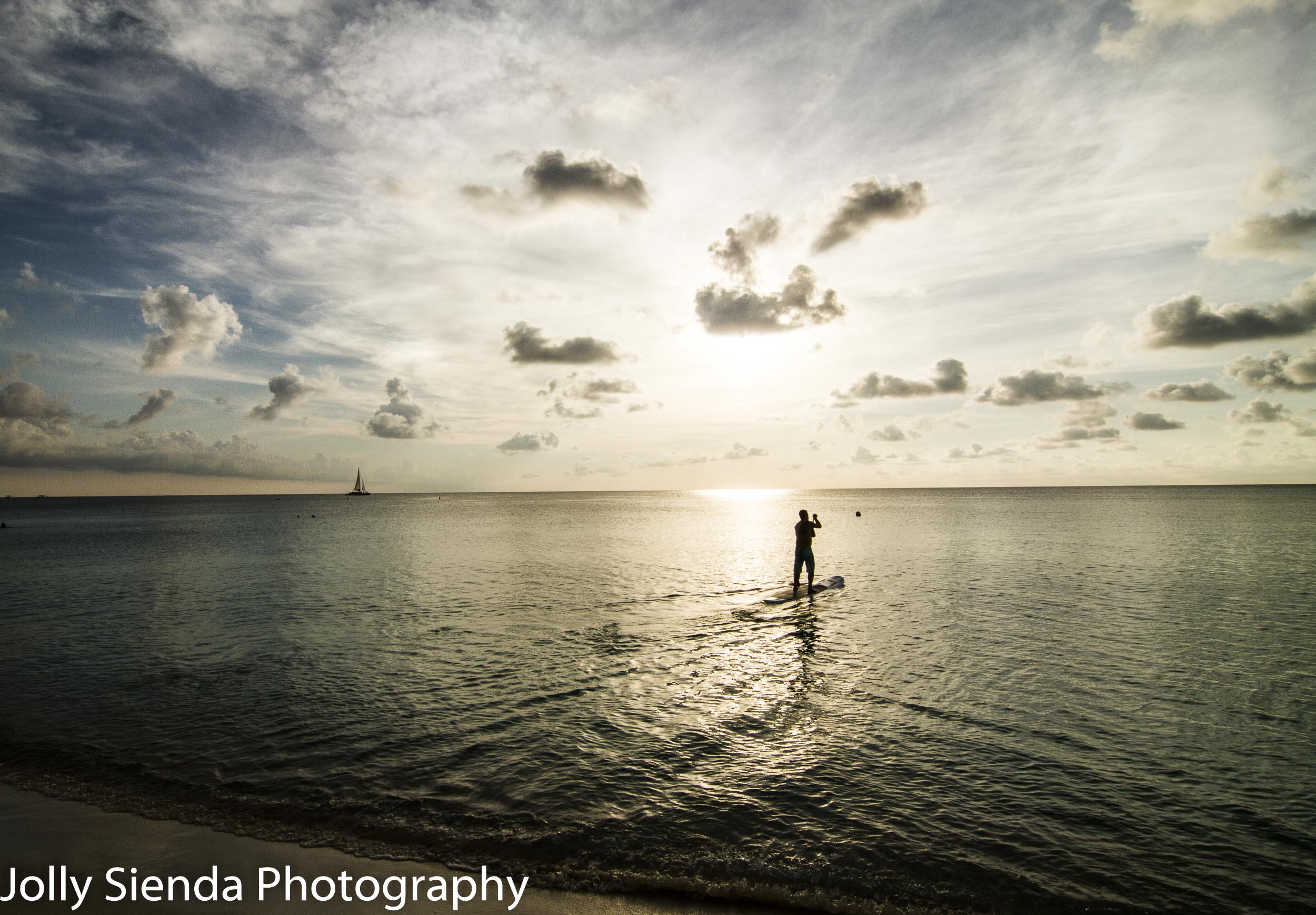 Paddle boarder rows out on the ocean to the sunset