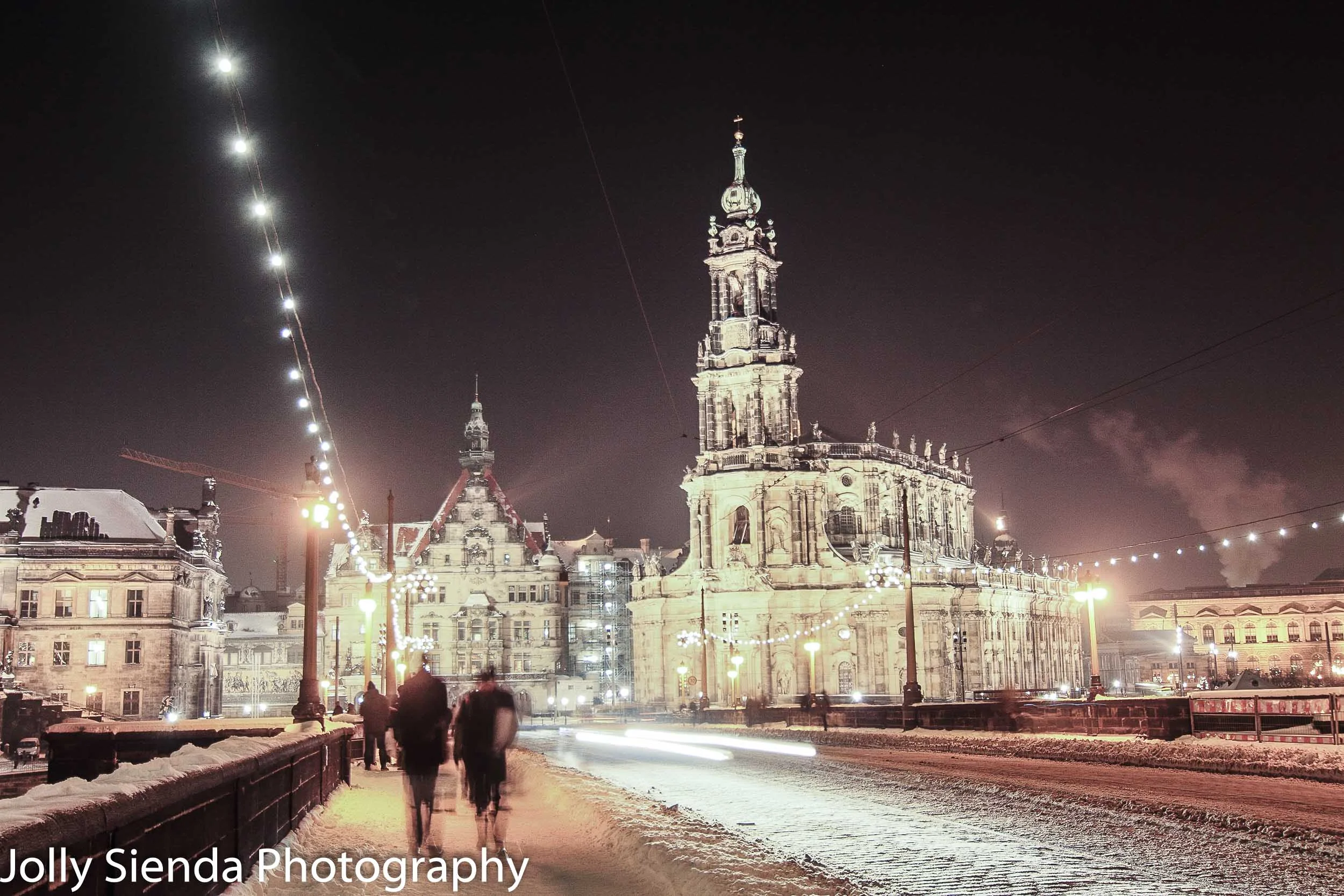 People walking across a snow packed Augustus Bridge, at night, w
