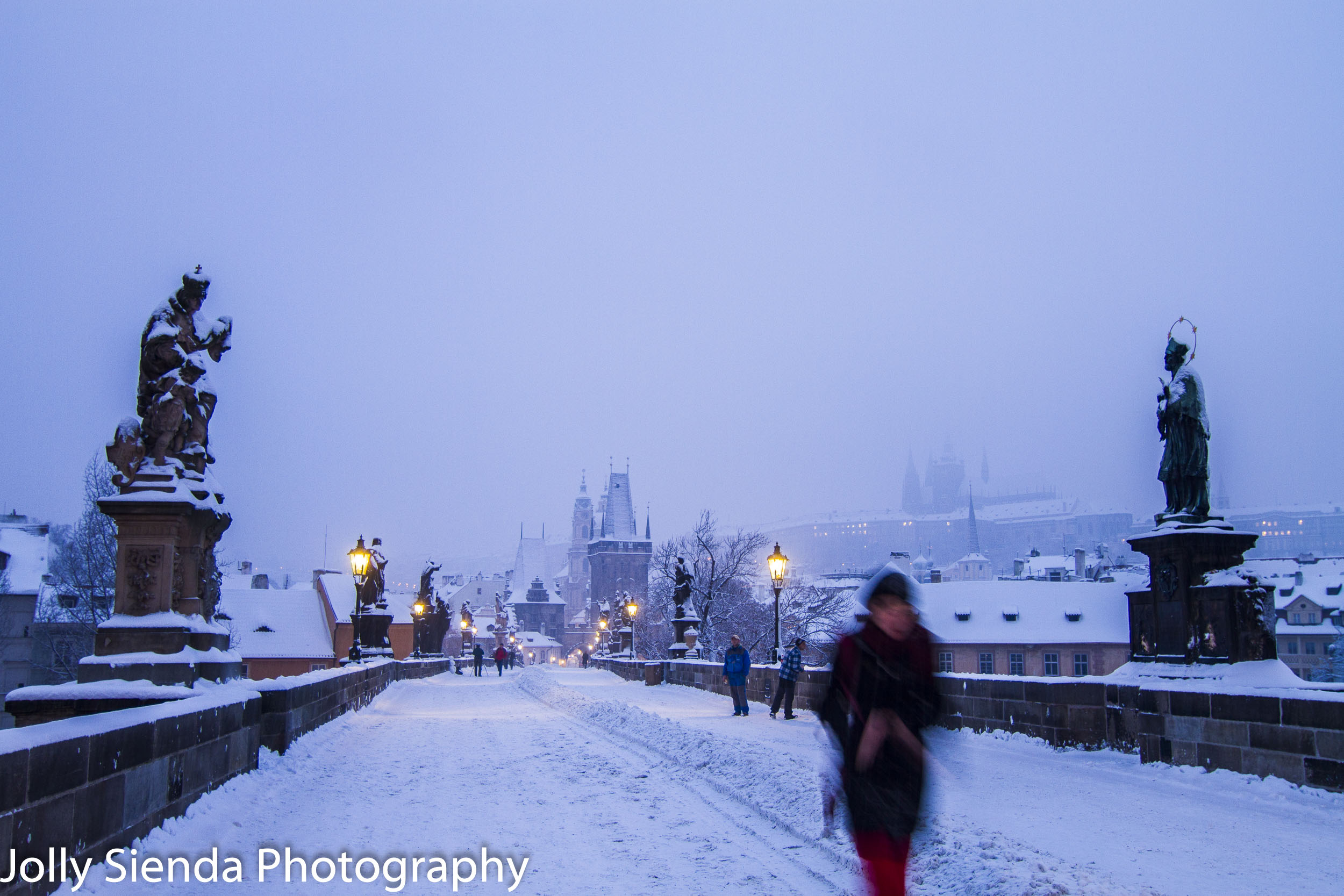 Woman in red crosses the Saint Charles Bridge while its snowing