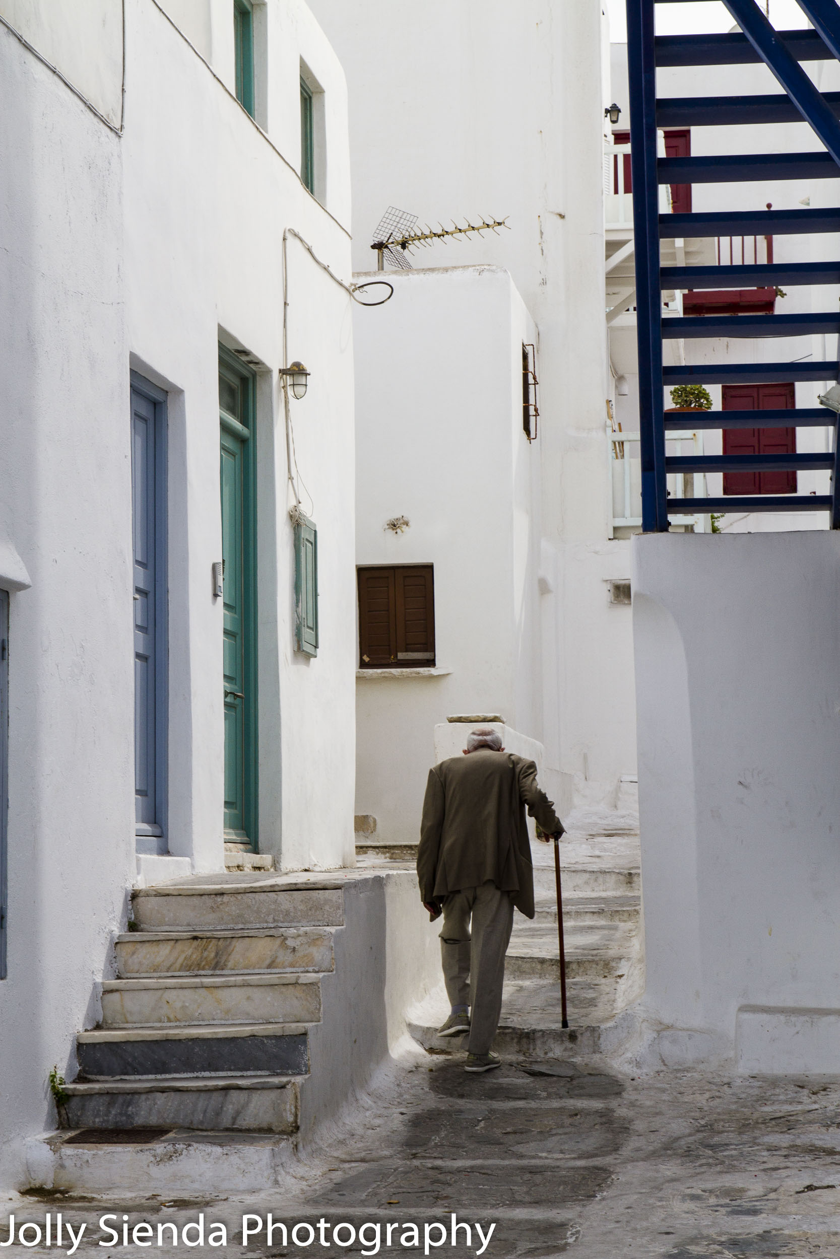 Elderly Man Walks with a Cane up Stucco Stairs in Mykonos