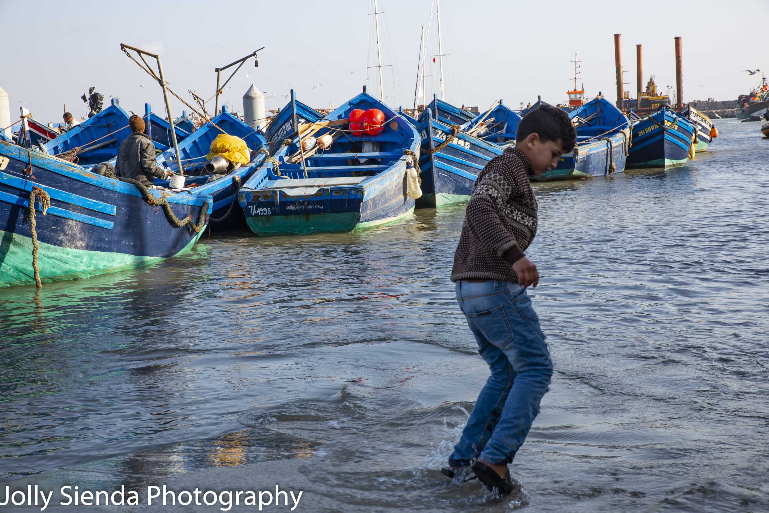 Boy plays in the water with fisherman and boats