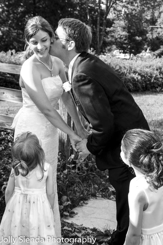 Groom kisses the bride as the flower girls look at them