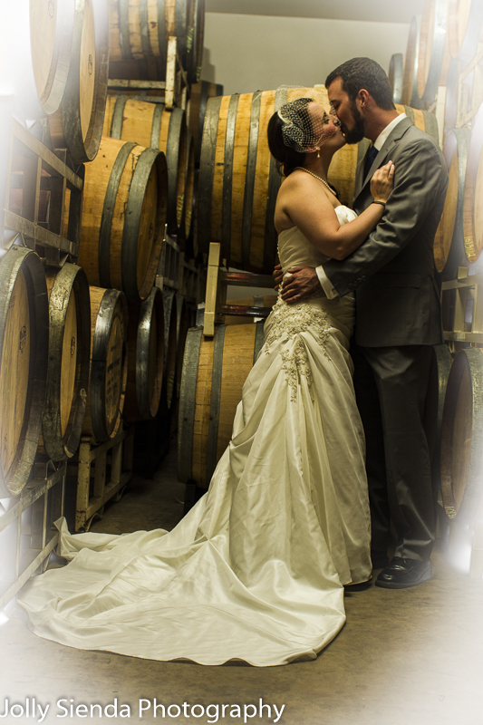 Bride and groom kiss next to wine barrels at the winery, wedding