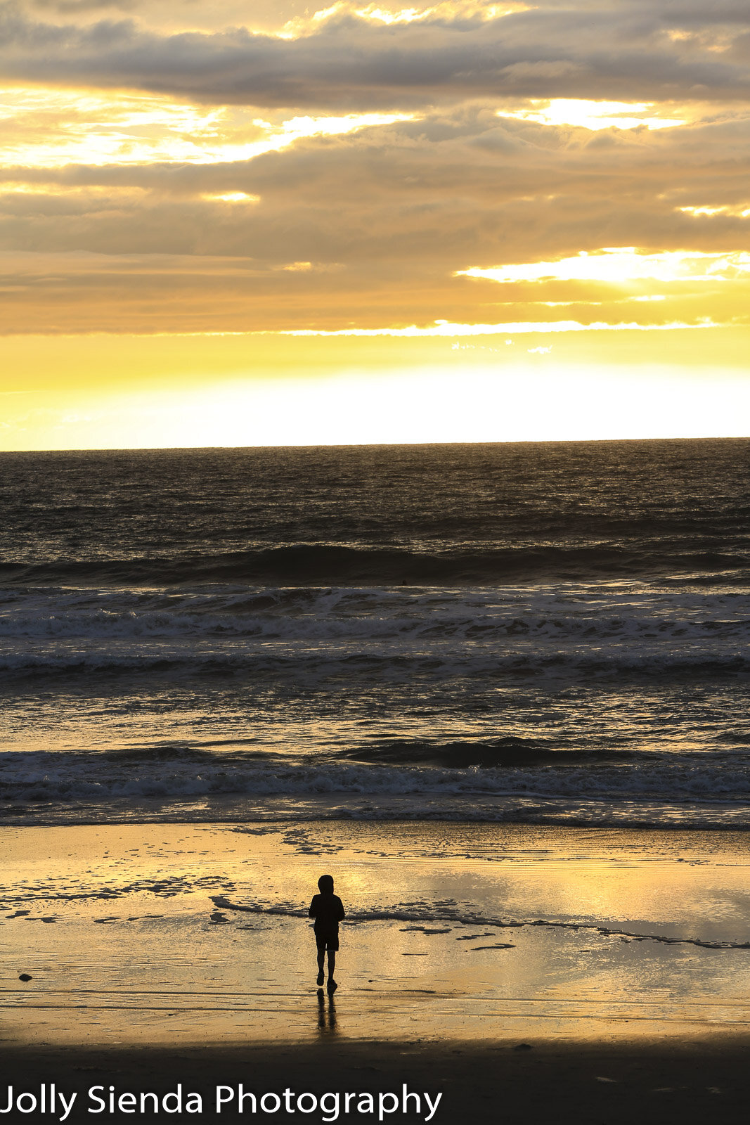 Person in a hoodie watches the sunsets glow on the sand at Torre