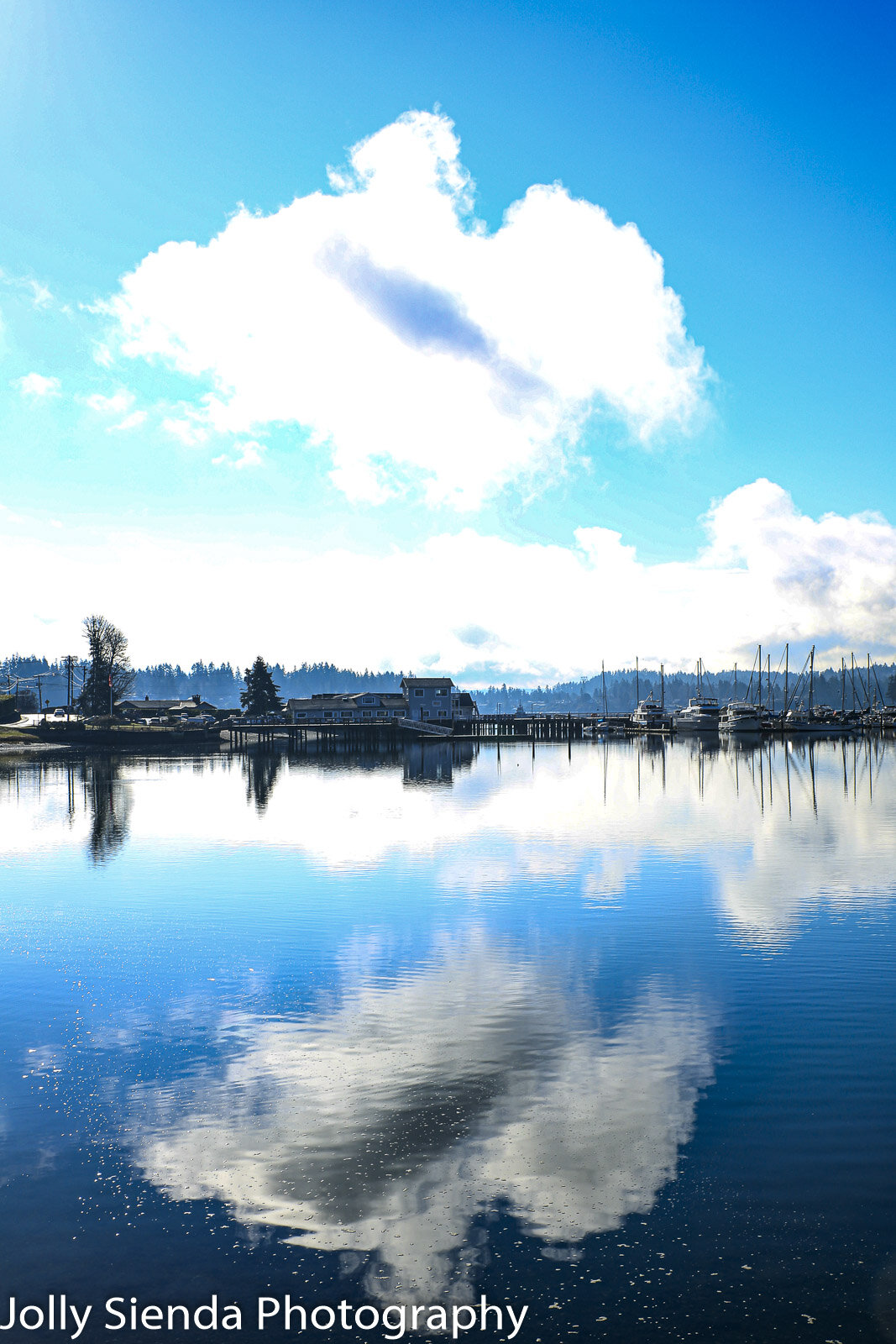 Large, white cloud reflects in the water near a boat marina