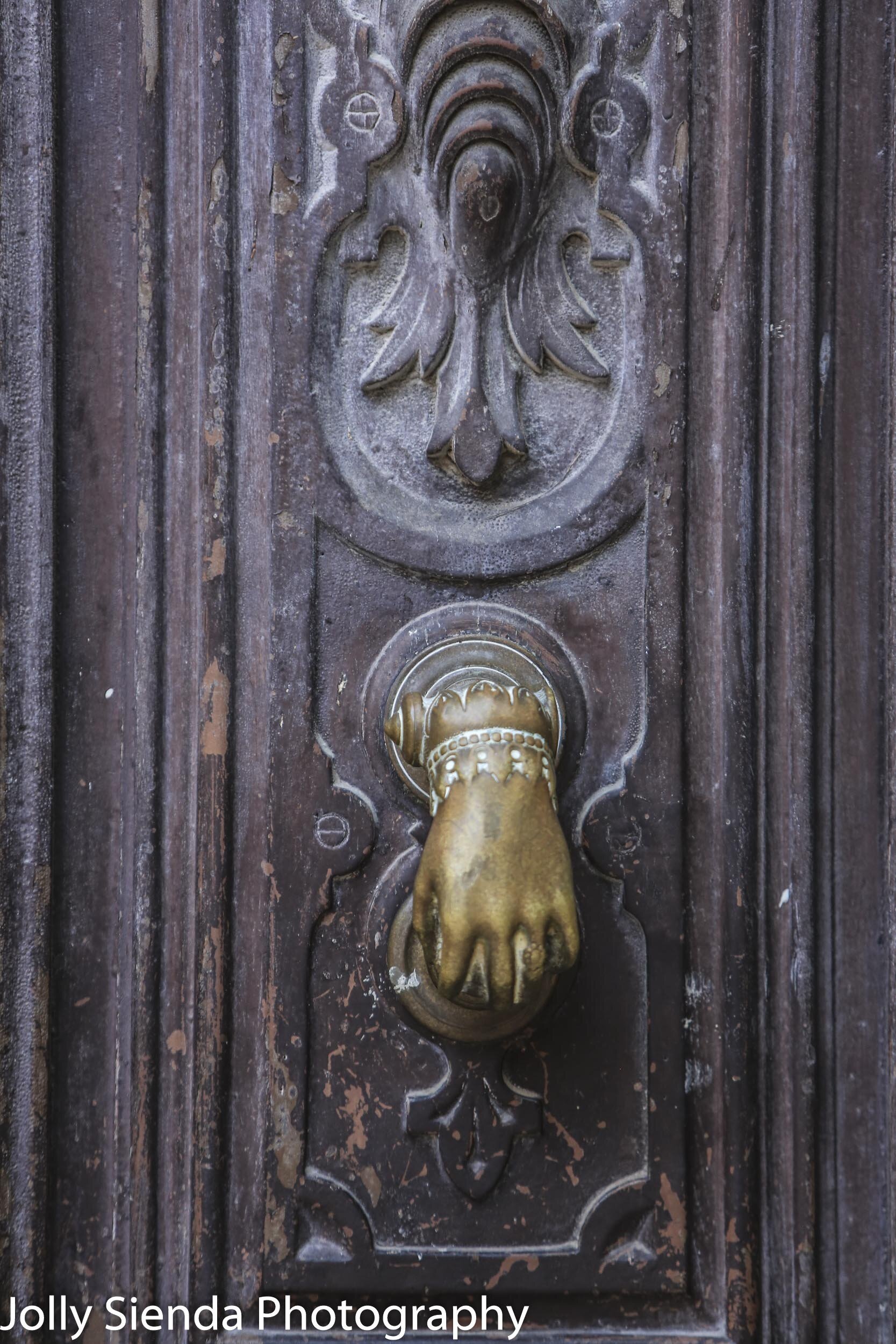 Brass hand door knocker on dark brown fleur de lis door
