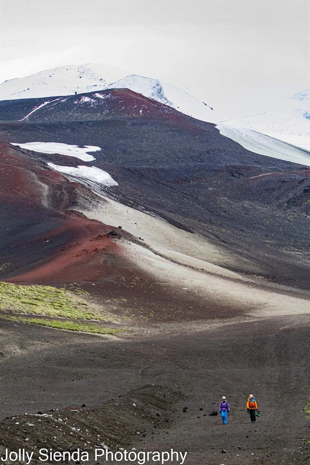 Snow shoe hikers hike down a snow capped volcano