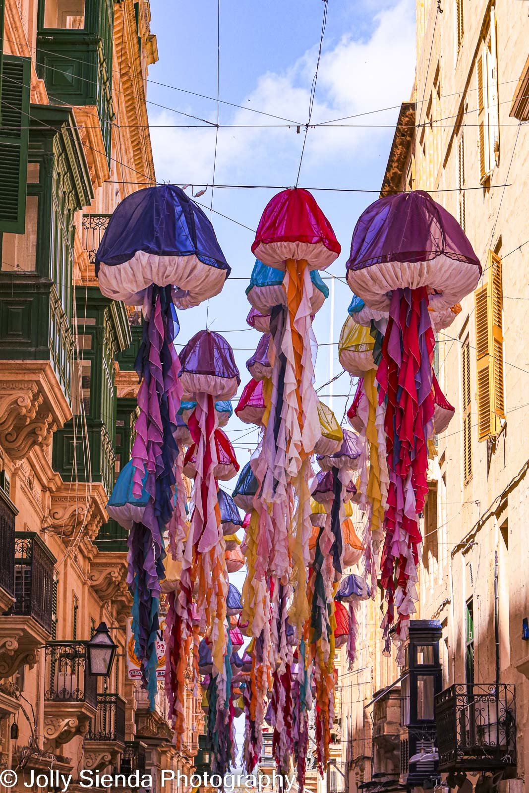 Cascading colored sea balloons hung narrow street with balconies