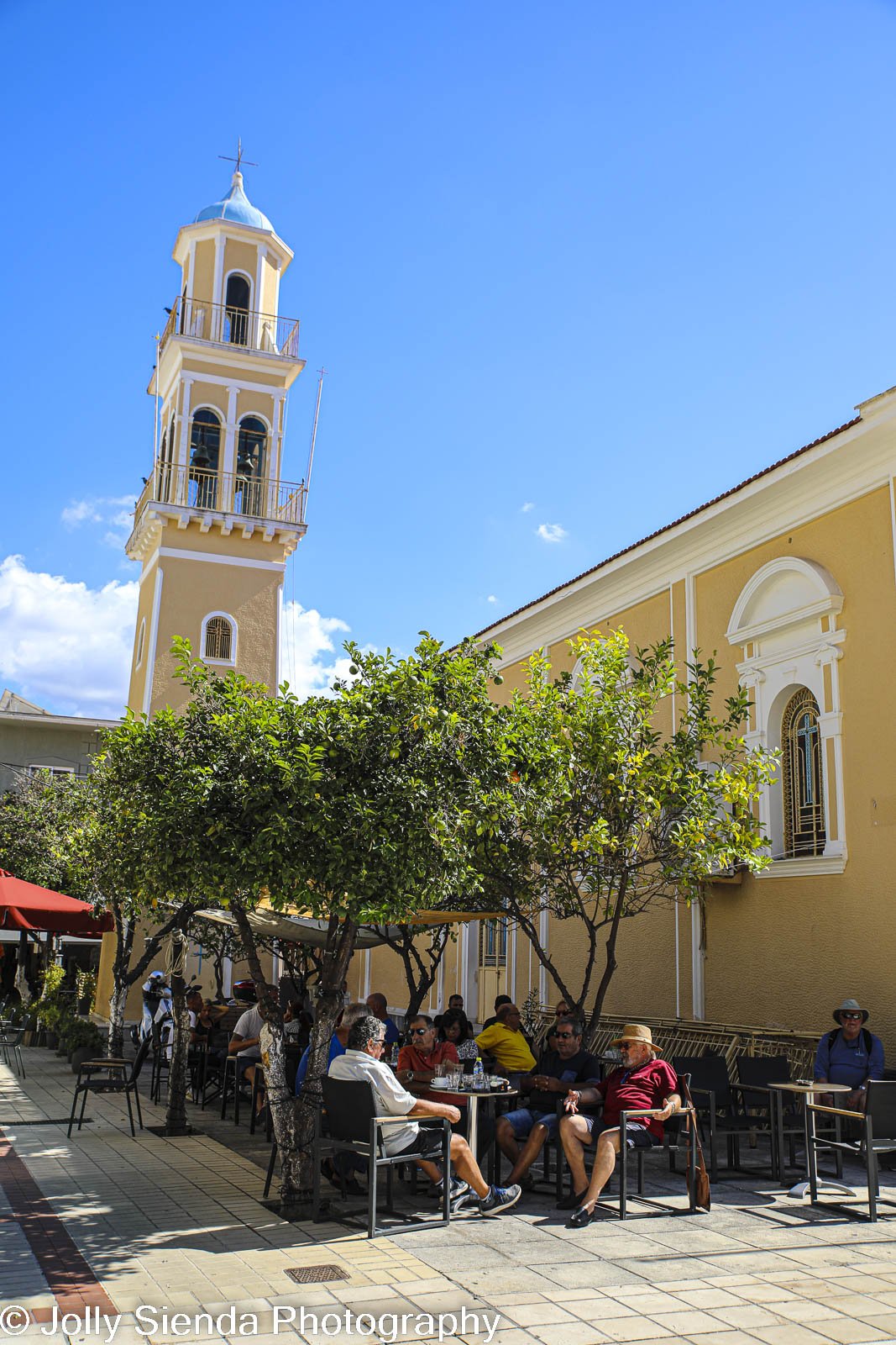 People at a cafe square and blue domed yellow Greek chuch