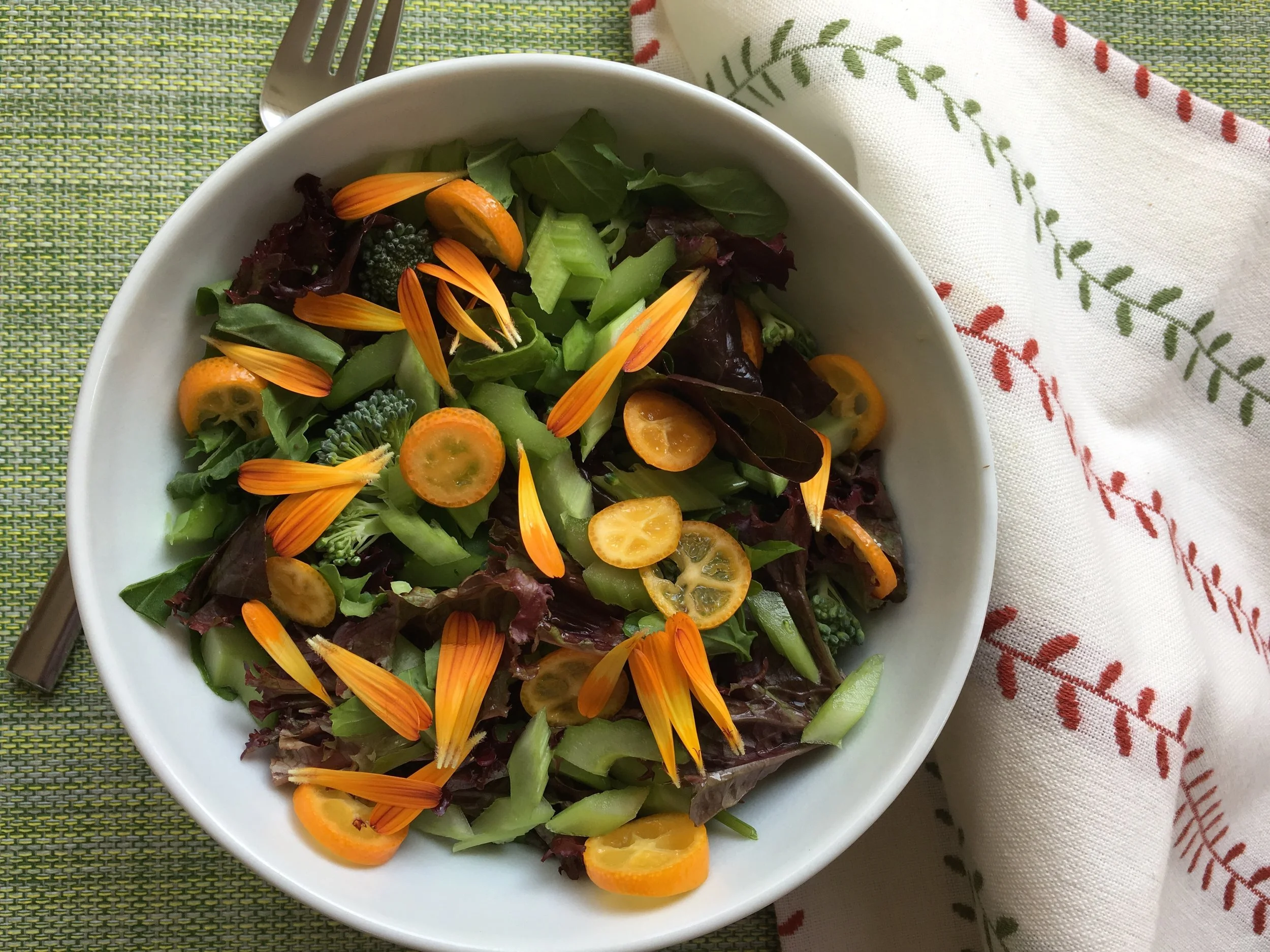 Kumquats in a winter garden salad with calendula petals, celery, broccoli, arugula and lettuce.