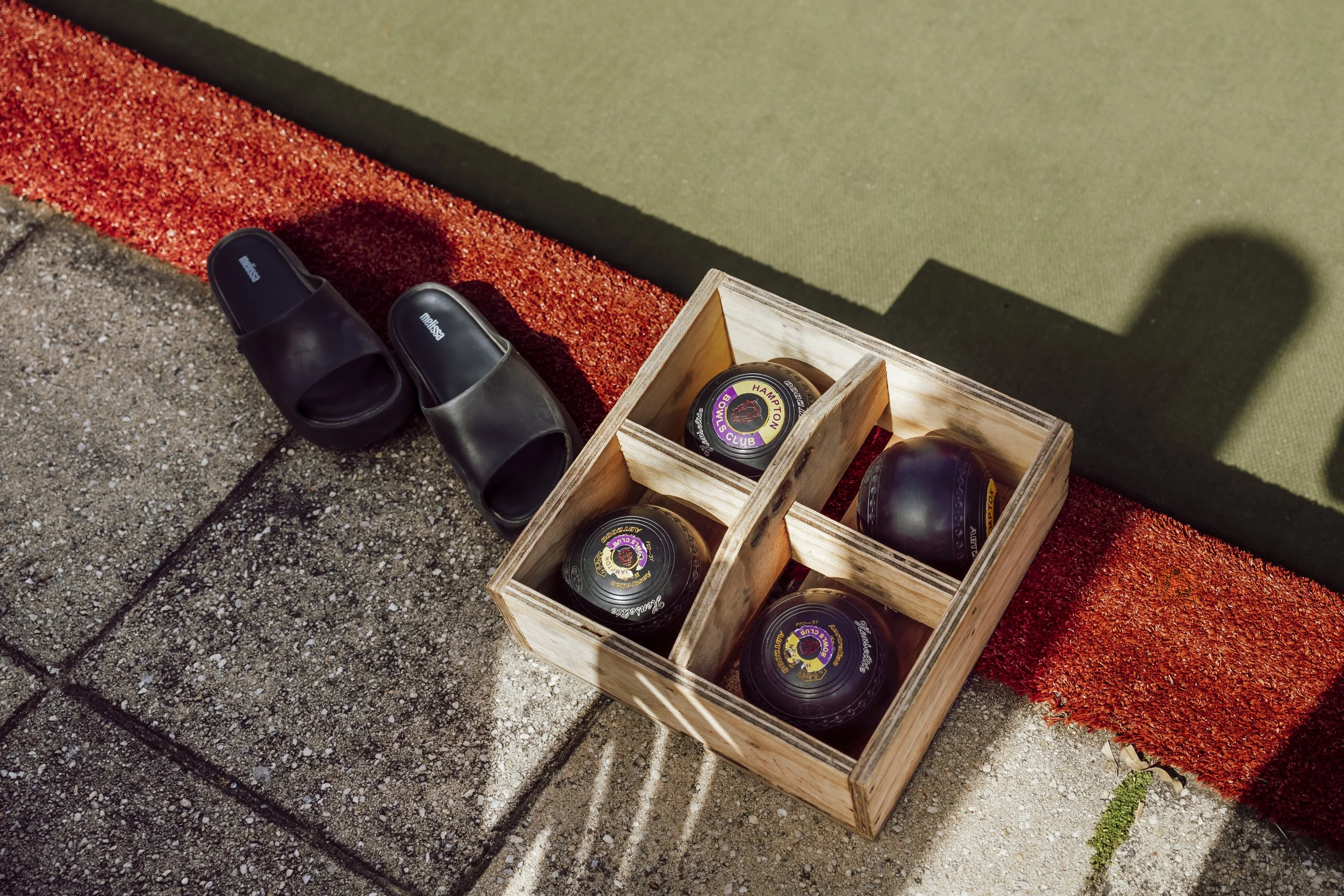 Lawn bowls in a wooden crate beside slip-on shoes at a barefoot bowls team event