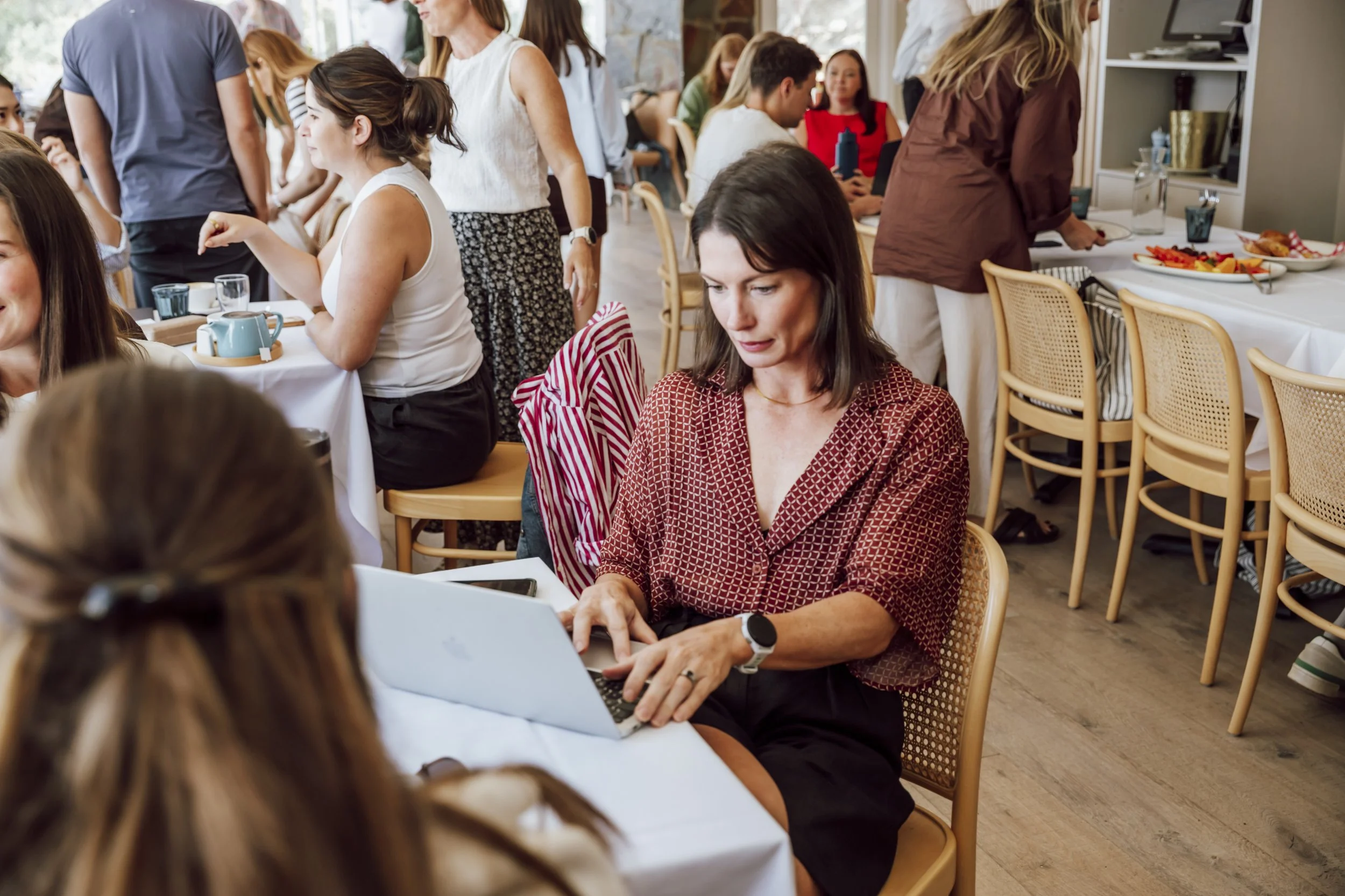 Team member working on a laptop while colleagues connect over morning tea at a corporate offsite