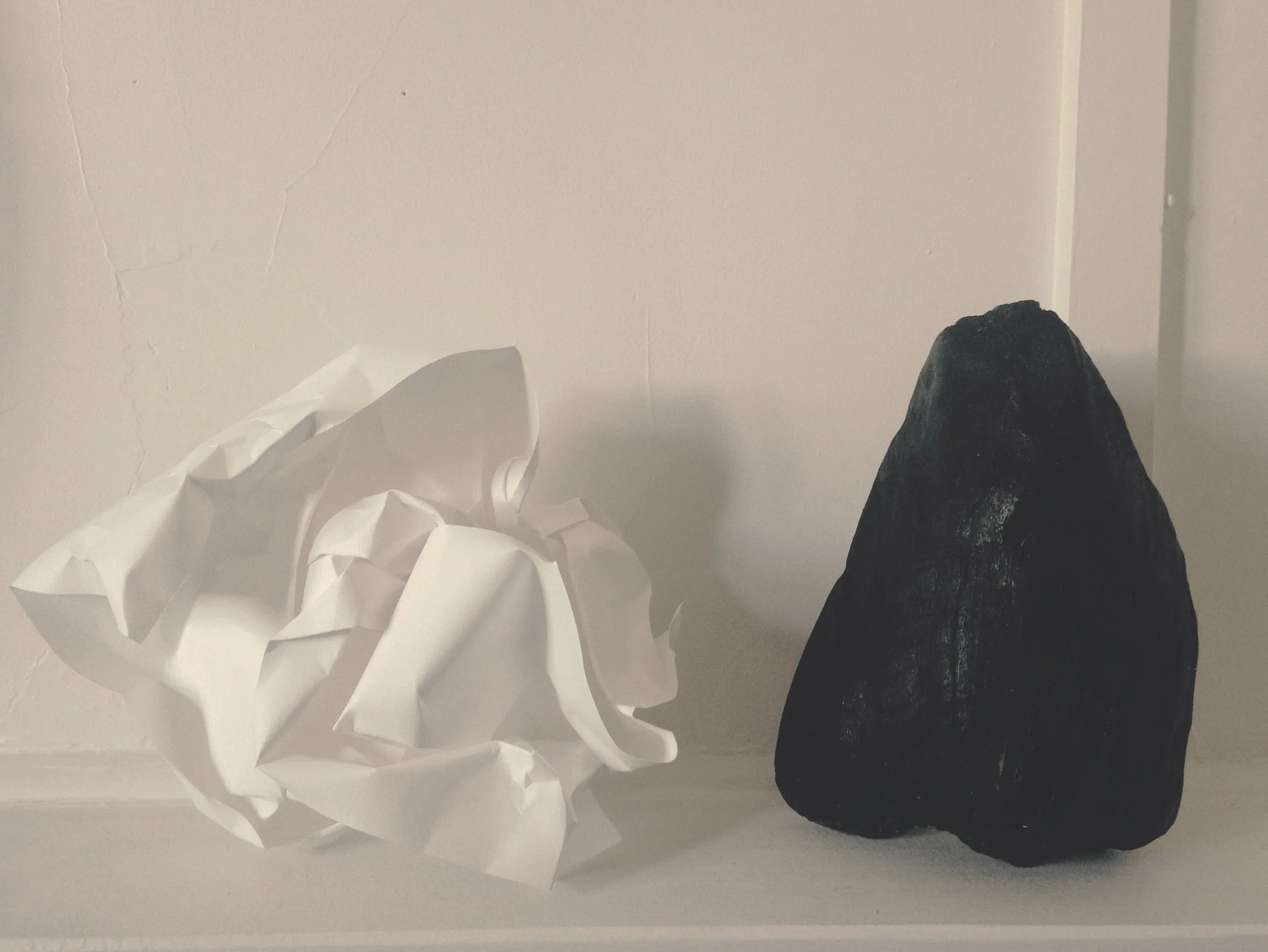 A large white crumpled ball of paper on the left next to a dark piece of wood painted black.