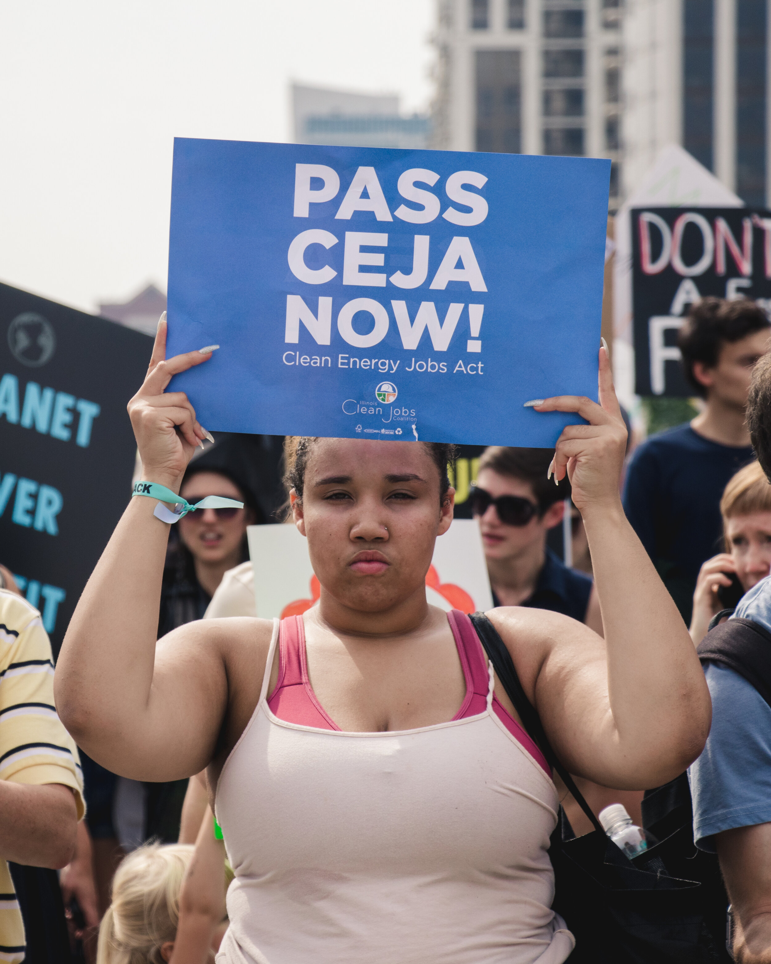  An organizer hold a sign above her that reads "Pass CEJA Now." The sign is a message for Gov. Pritzker to sign the Clean Energy Jobs Act that would commit Illinois to rely on 100% renewable energy by 2050. 