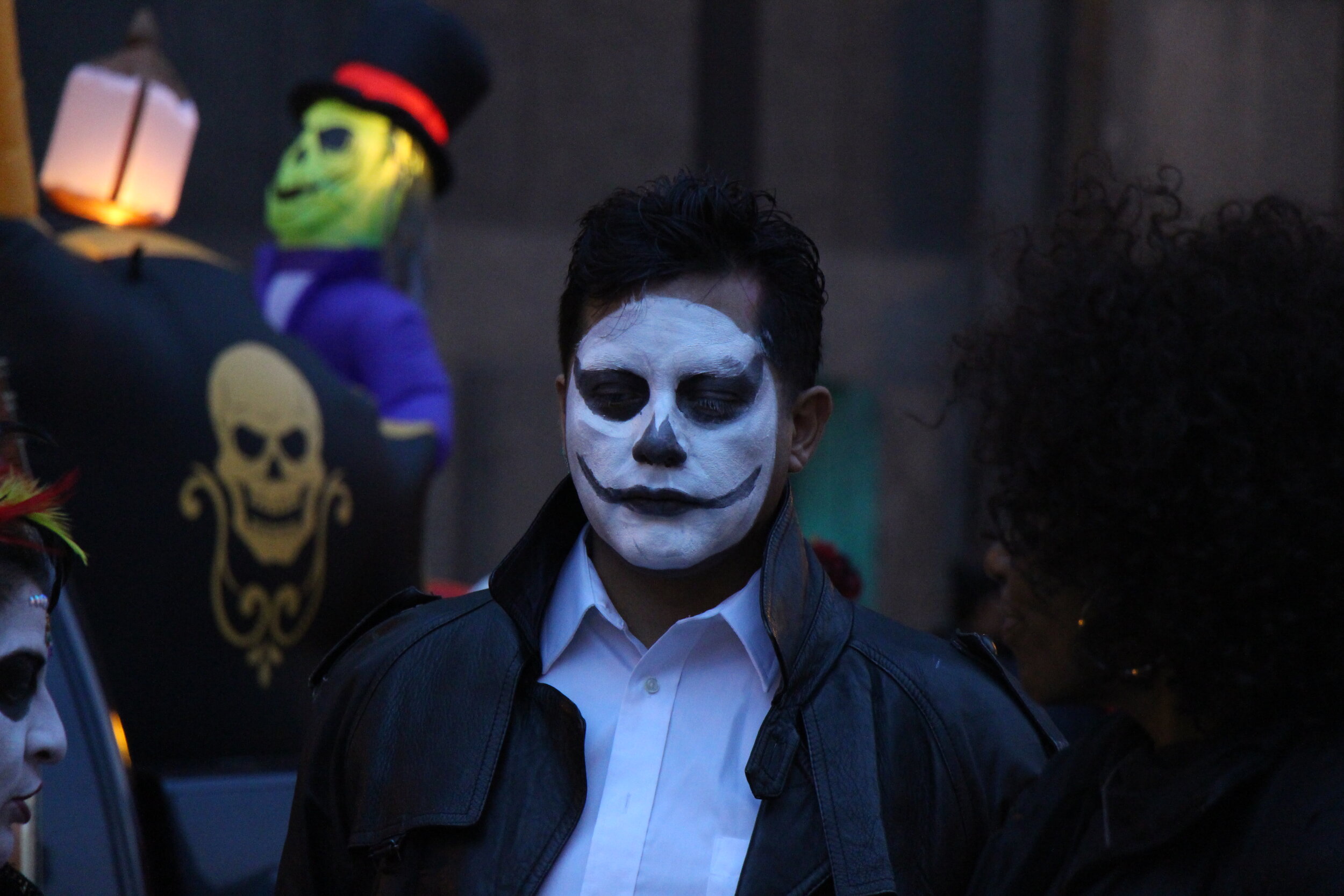 A young man at the Art in the Dark parade with his face is painted white and his eyelids and lips are covered in black .