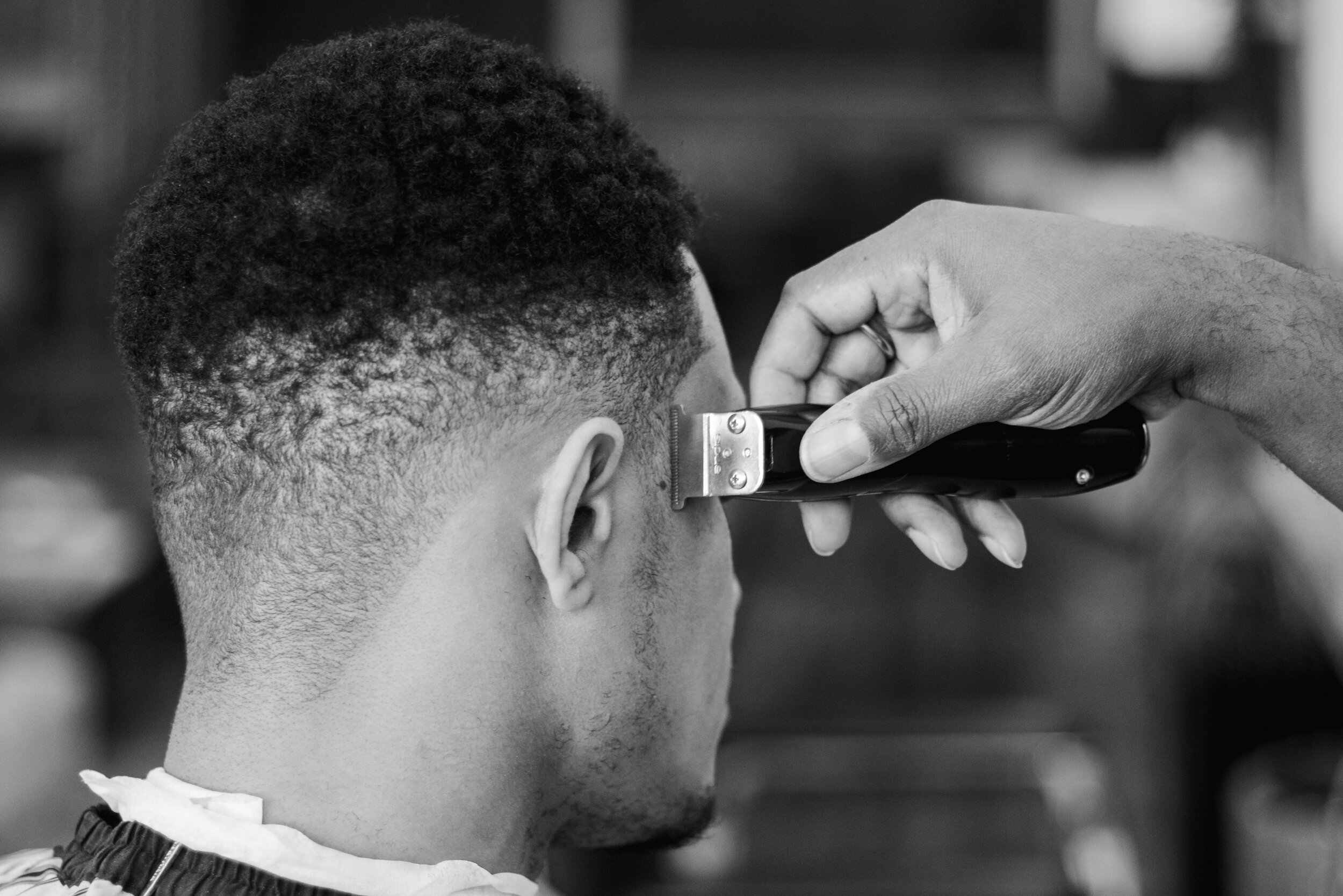  Owner and barber Bobby Price trims the overgrown hair on the side of a customer's head into a fade, a hairstyle that is longer on the top than it is on the bottom. 