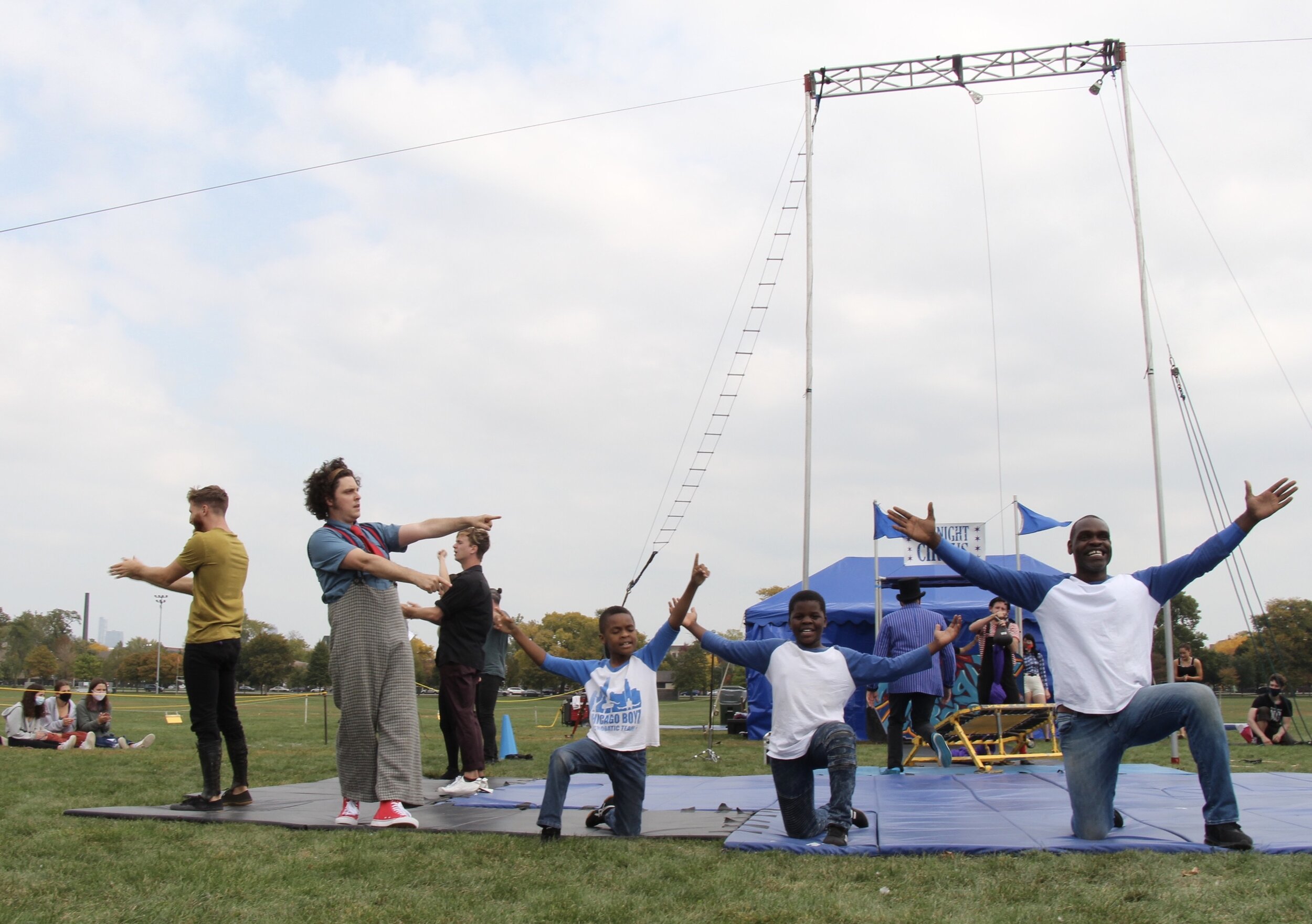  The Chicago Boys in white/blue take a bow in front of the audience as circus artists engage with the crowd smiling and clapping.(Photo taken by Sabrina Hart) 