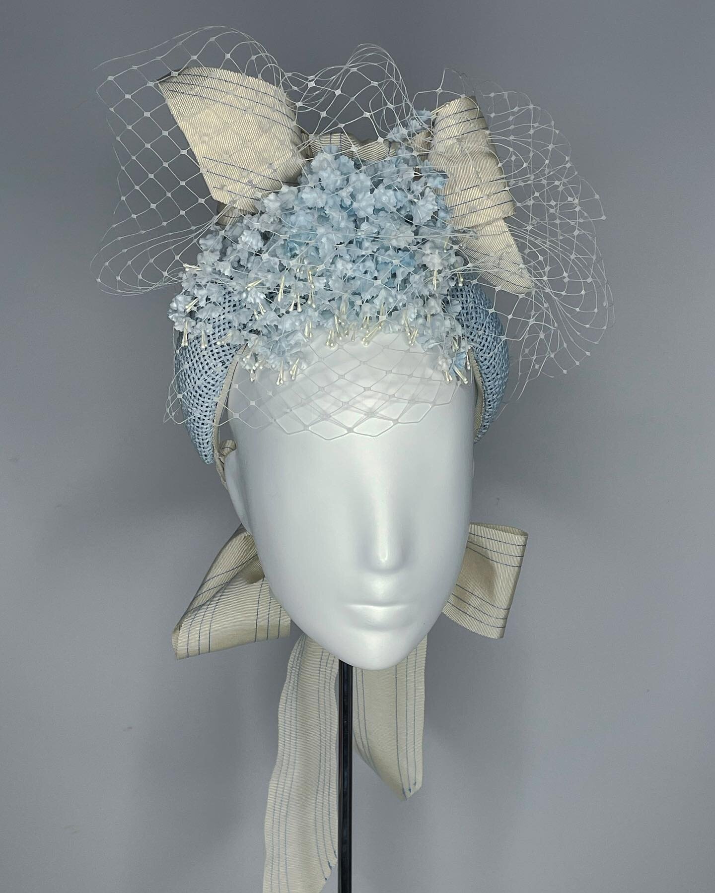 How about this little number? 
This open textured straw hard and is in the prettiest shades of blue and is peppered with the daintiest of Japanese silk flowers. And for added drama, there is are double bows one on top and one at the neck. 

Available