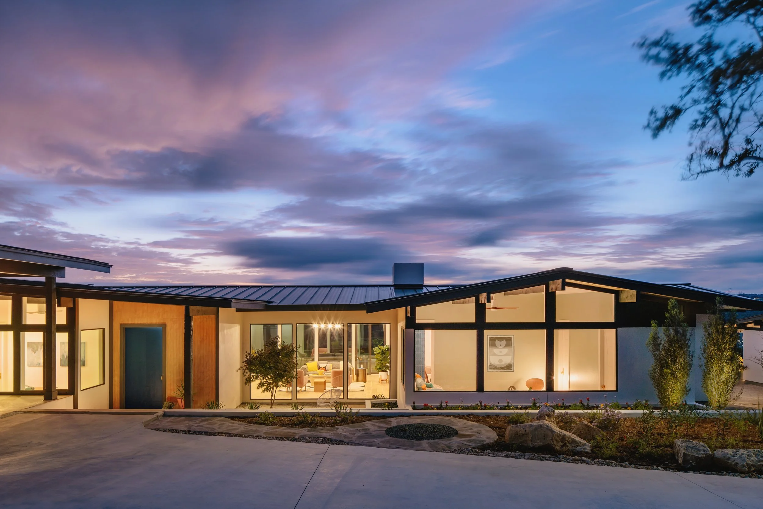 Midcentury modern ranch exterior glowing with warm light at dusk, Breathe Design Studio