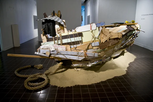 “Yet I Trust the Sanity of My Vessel”, 12’x5’x7’. Scrap wood, ceiling fans, cupboards, bicycle tires, aluminum roofing, ironing board, window panes, rope, plastic bags, twine, sand. 