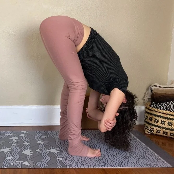 Dark haired yoga teacher demonstrating standing forward fold with bent knees