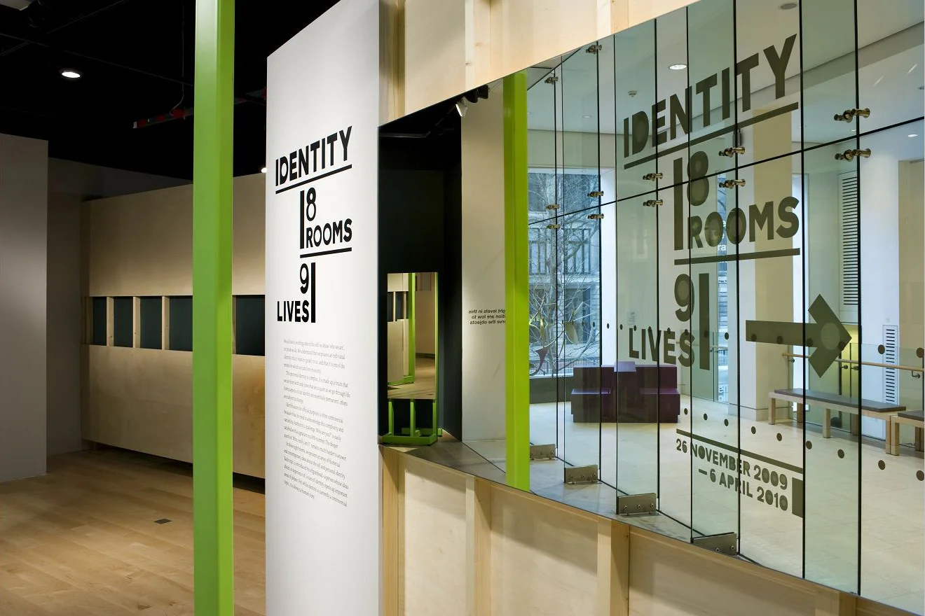 Exhibition installation with the title "Identity: 8 Rooms, 9 Lives".