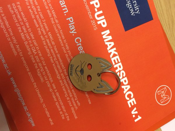 A keyring in the shape of a cat’s face displayed on the orange Makerspace leaflets