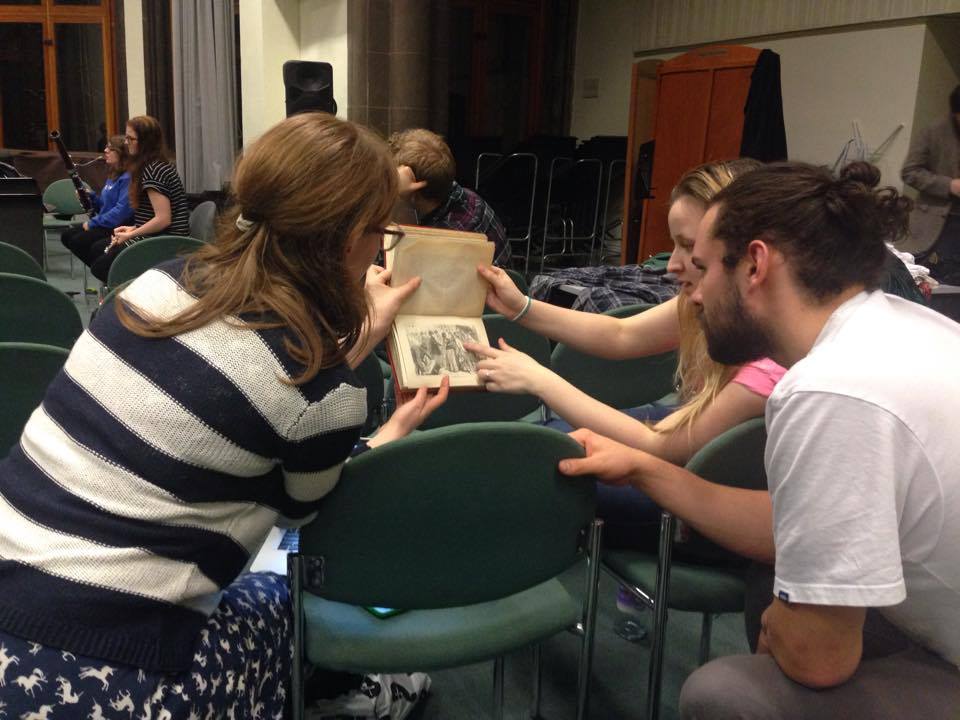 Three people examining an old printed copy of The Mystery of Edwin Drood .