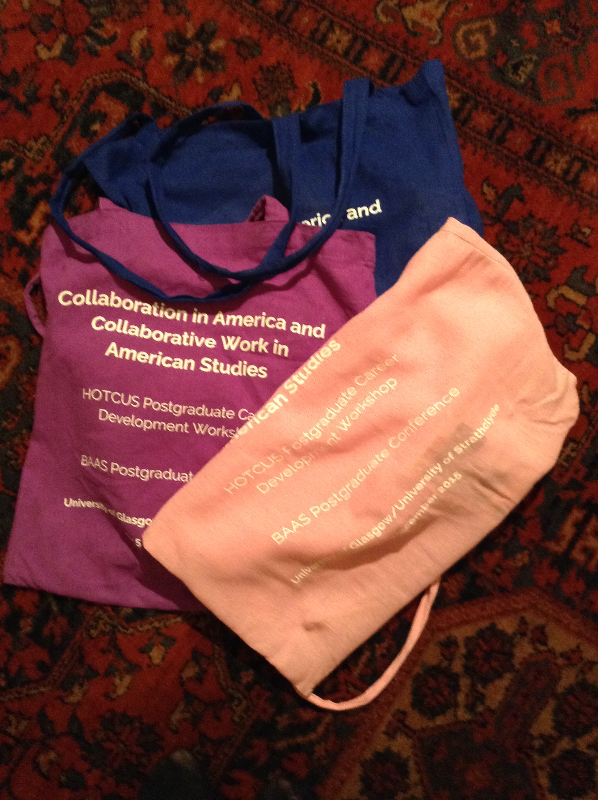 Three conference tote bags in navy, purple and peach. Conference details are printed on the badges.