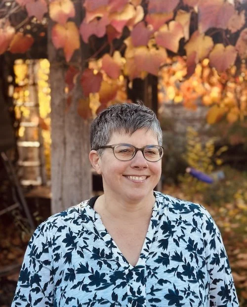 Wendy Allen in her garden with autumn orange vine leaves in the background