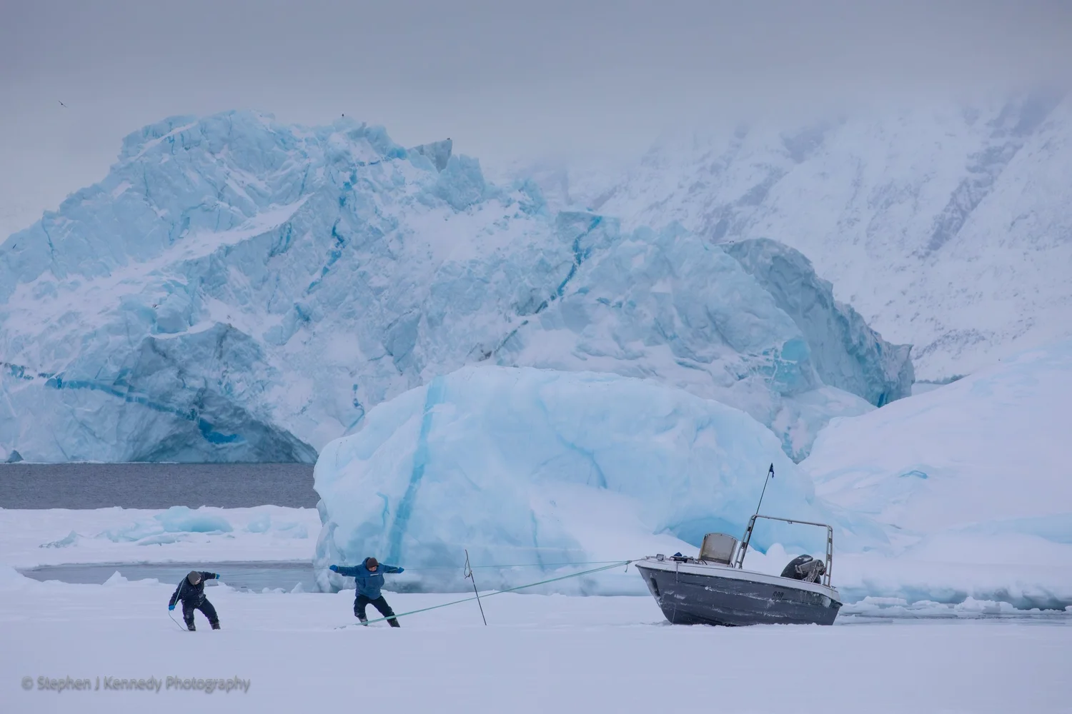 Uummannaq — harbour in snow, men hauling boat onto ice