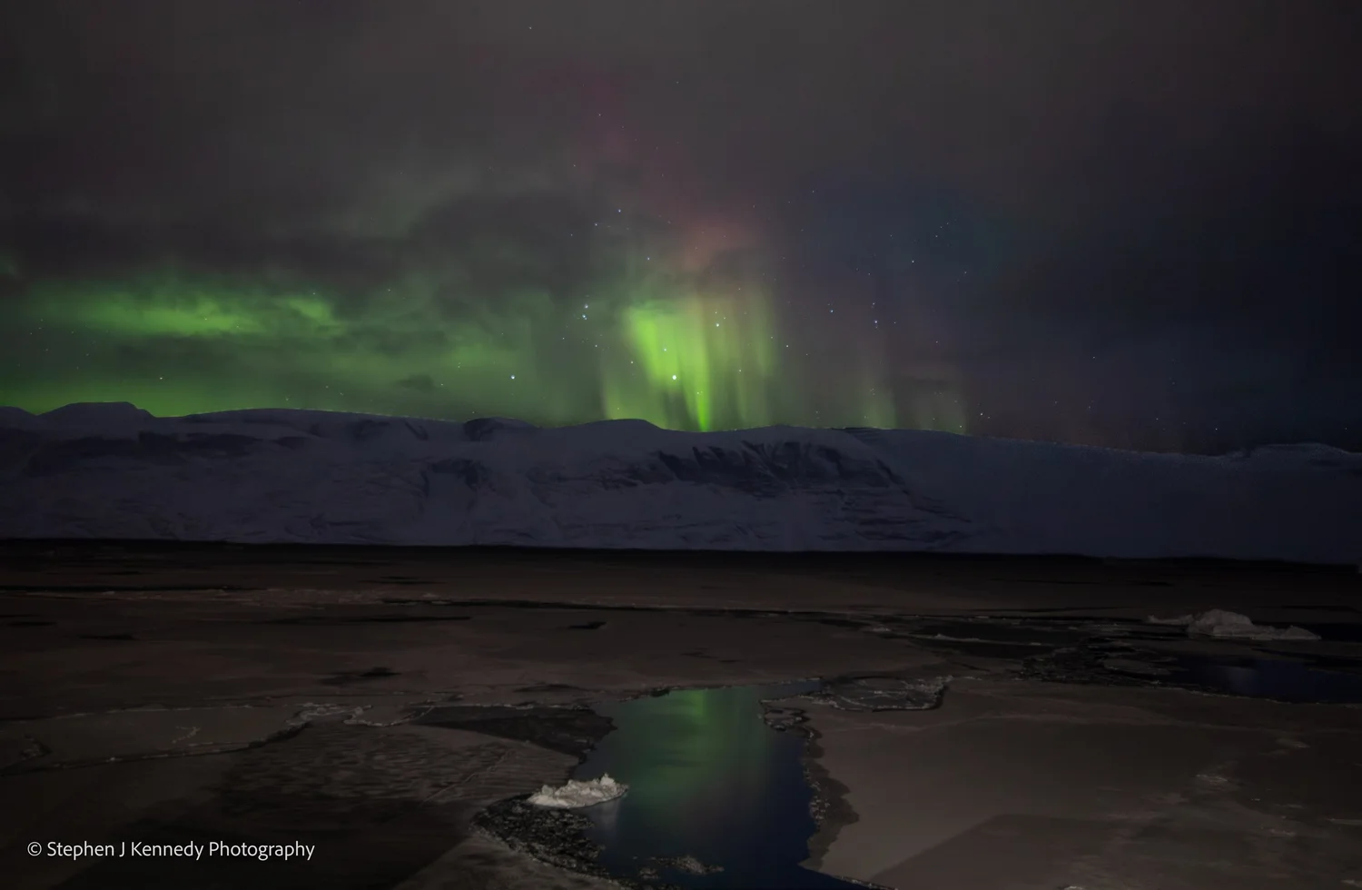 Uummannaq — aurora to the south horizon over icebergs