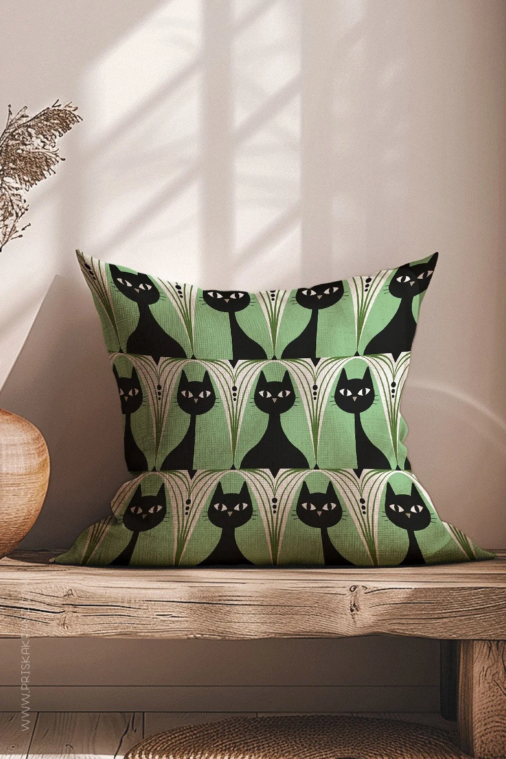 Decorative pillow with a bold mid-century–inspired pattern of black cats on a soft green background, styled on a wooden bench in natural light
