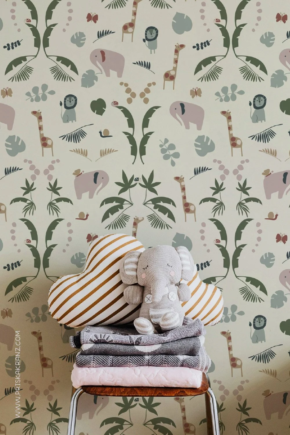 Wallpaper with a whimsical jungle design in soft neutral colors, featuring illustrated lions, elephants, giraffes, leafy palms, and simple foliage on a creamy background, shown installed on a wall above a light wood floor.