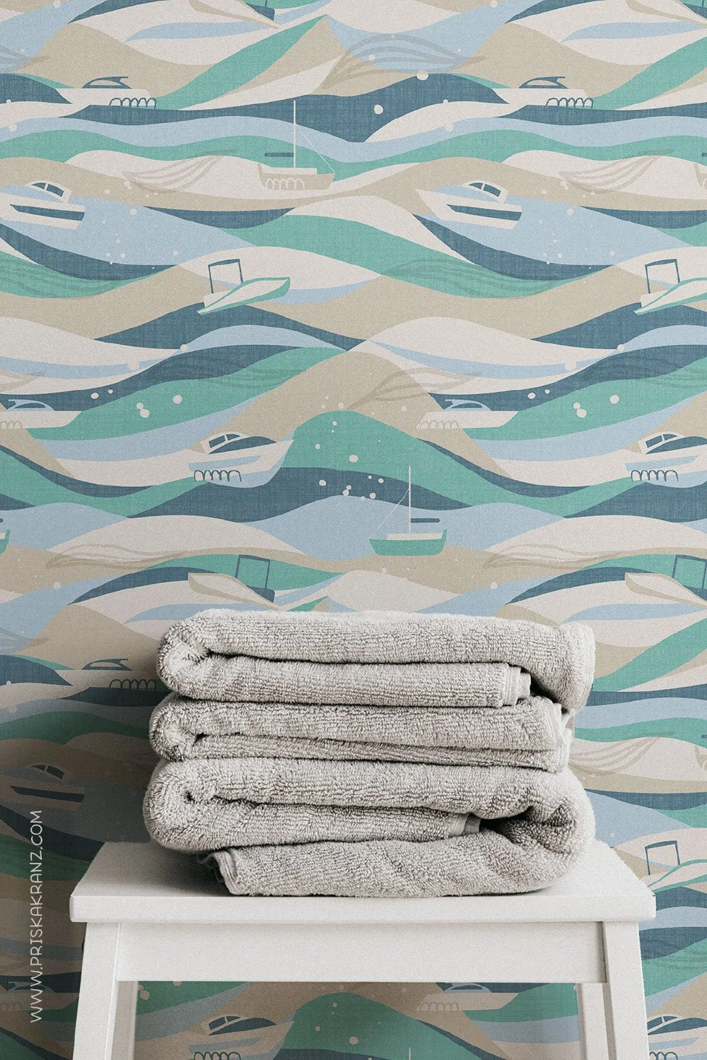 Coastal wallpaper with stylized ocean waves and small boats in soft blue, sage green, and sandy tones, styled behind folded neutral towels on a white stool.