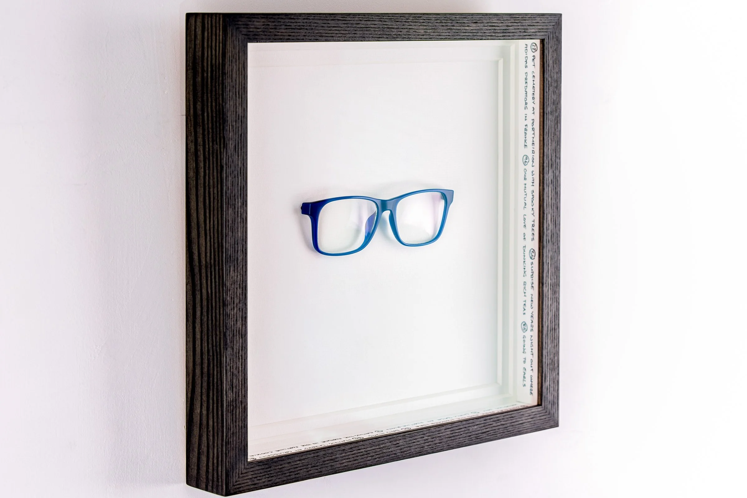 Object framing of spectacles with written memories on the internal spacers. Double mounted framed in stained ash wood and AR70 glass Framed by The Nunhead Framer in Nunhead SE15 London