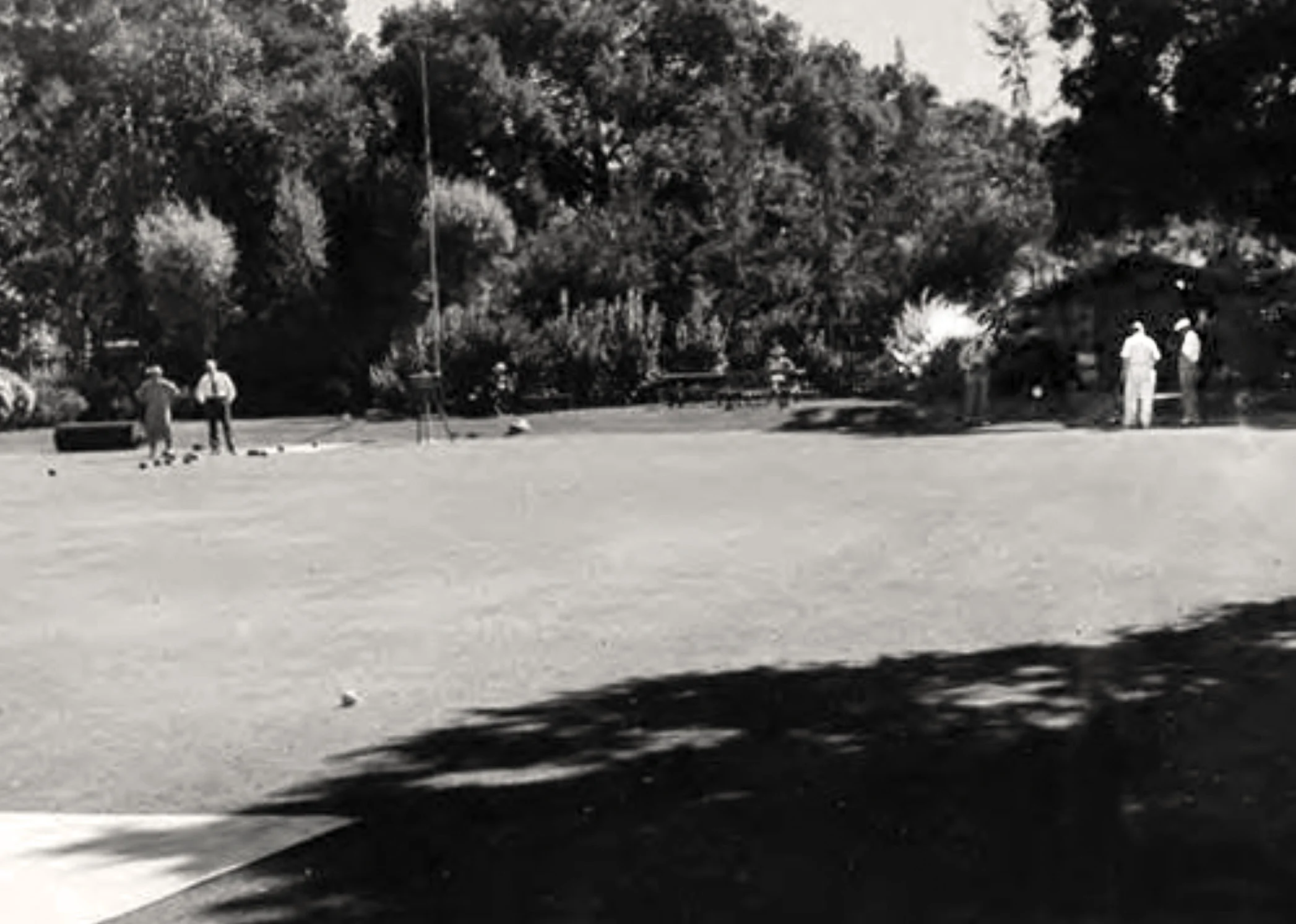 The green about 1936 looking towards where the clubhouse stands today. The old flagpole is just visible in front of the trees to the left of the figure seated center left. The original shed is behind the two bowlers to the right. Note the sloping bank behind the green. There also appears to be a roller on the green to the left. PAHA photo.