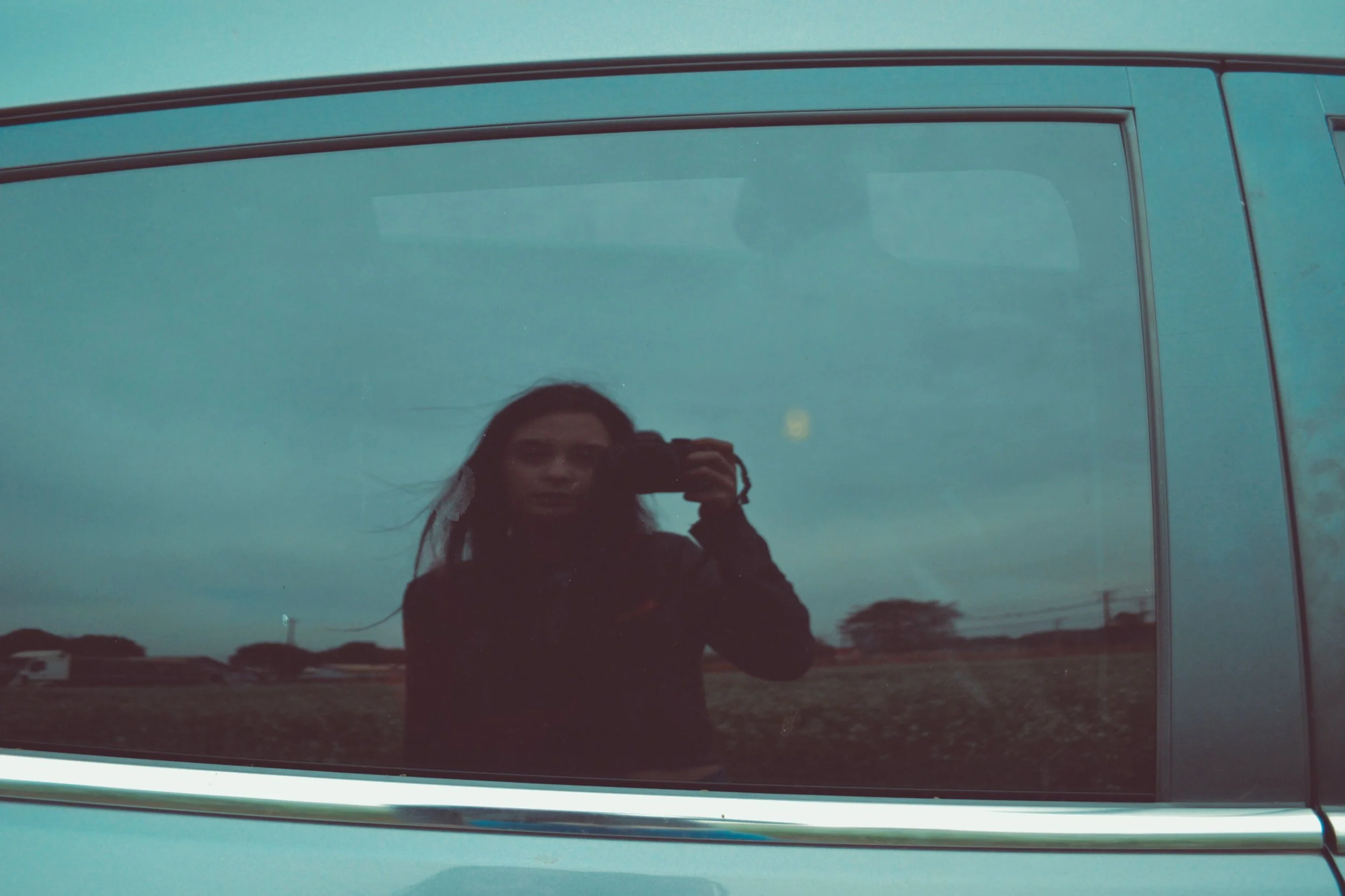Reflection of a photographer holding a camera in a vehicle window before a client session, highlighting photography business travel and bookkeeping.