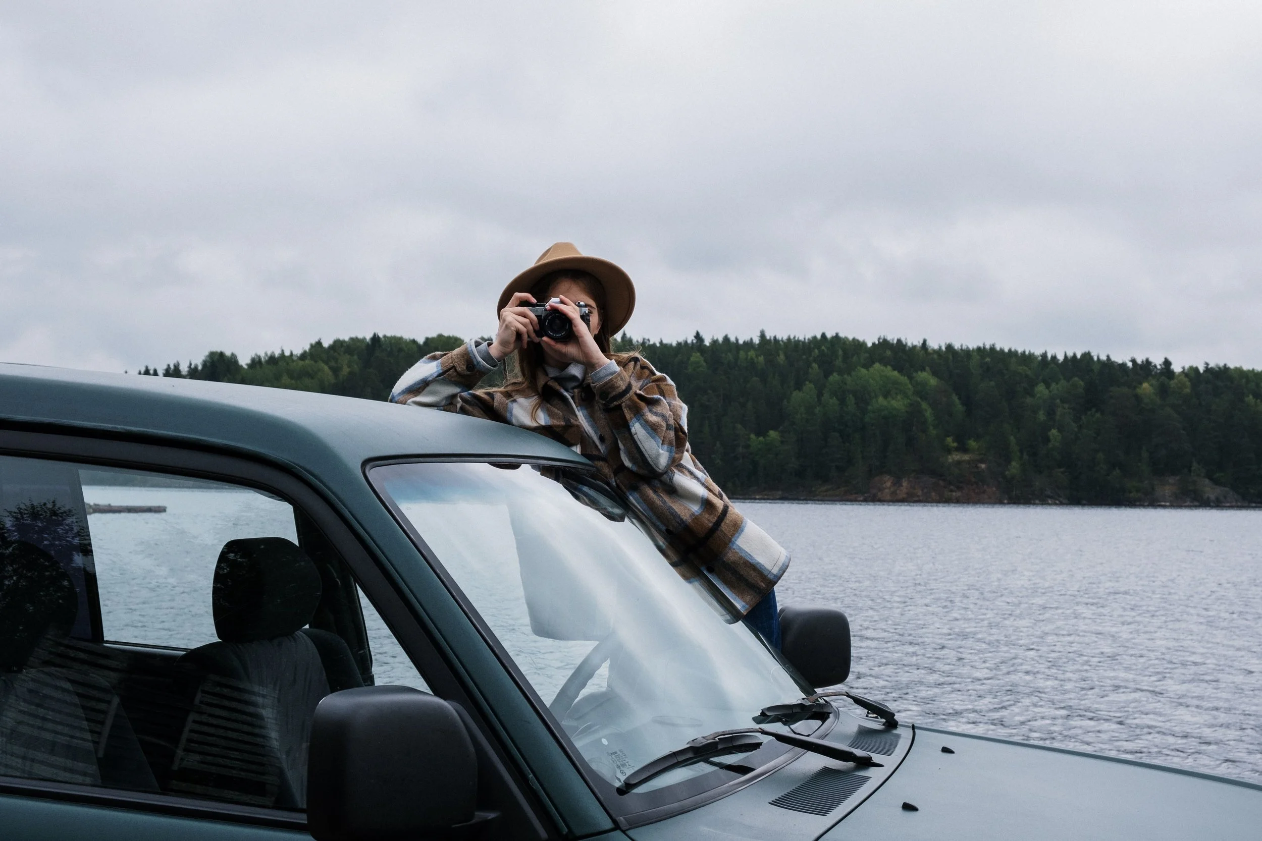 Photographer taking photos beside a parked vehicle at a lakeside location, illustrating business travel and mileage tracking for a photography business.