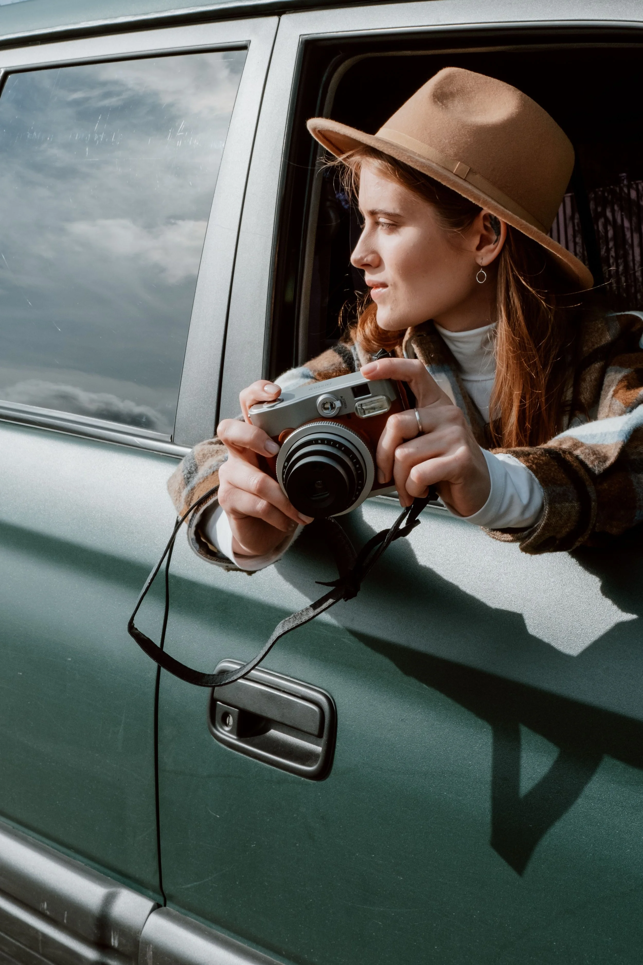 Photographer holding a camera from a vehicle window while scouting a photo session location, representing standard mileage deductions for photographers.