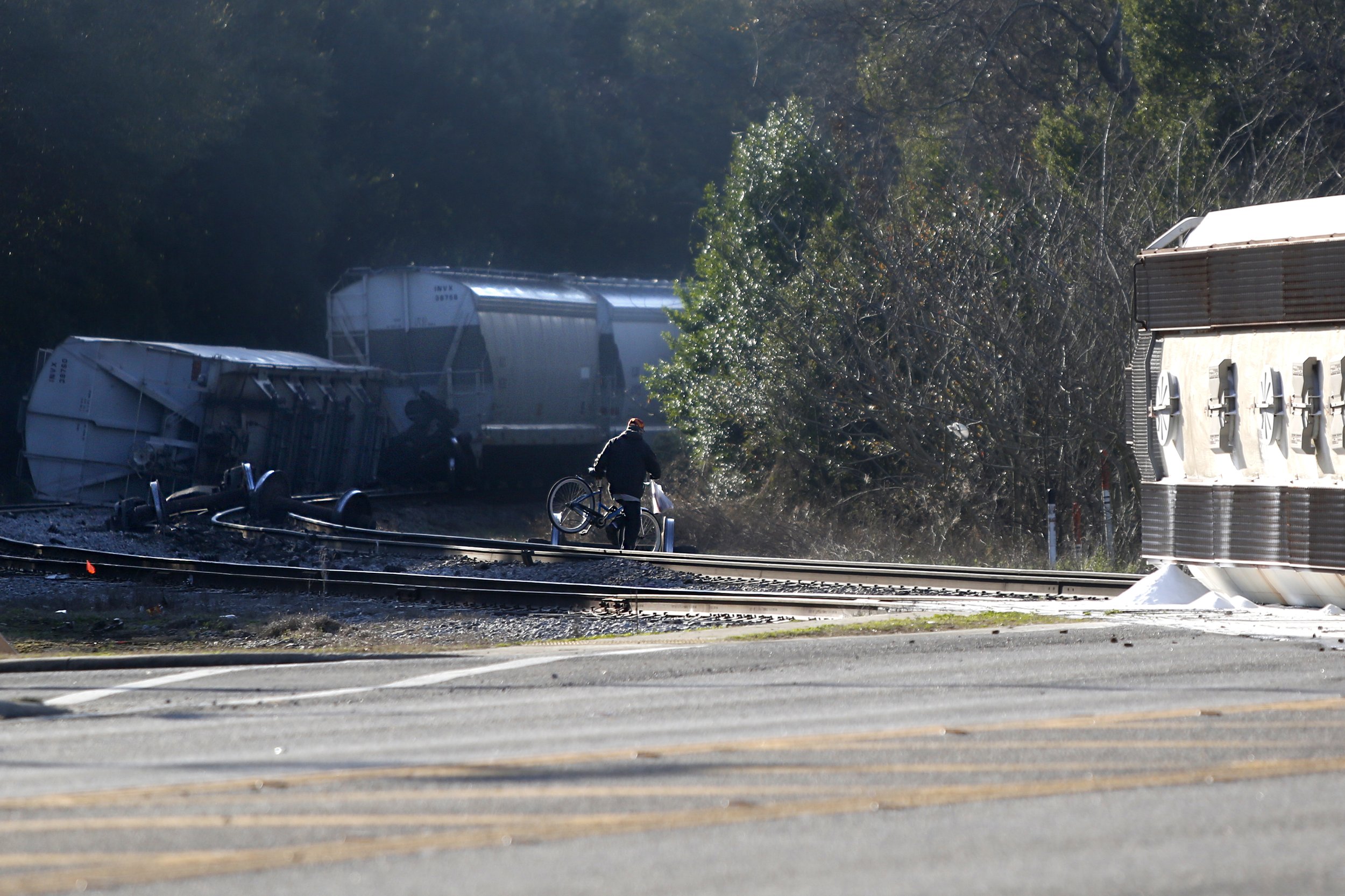  A man crosses the tracks with his bike between two parts of a derailed train in downtown Quincy, Fla., on Jan. 30, 2018. Two of the train’s seven cars derailed, spilling their cargo of adipic acid.  