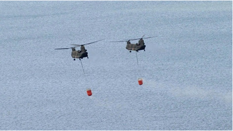 Two Japanese Ground Self-Defense Force helicopters hover over off Natori, Miyagi Prefecture as they carry seawaters to drop onto the tsunami-crippled Fukushima Dai-ichi nuclear plant Thursday, March 17, 2011. (The Yomiuri Shimbun / Kenji Shimizu)
