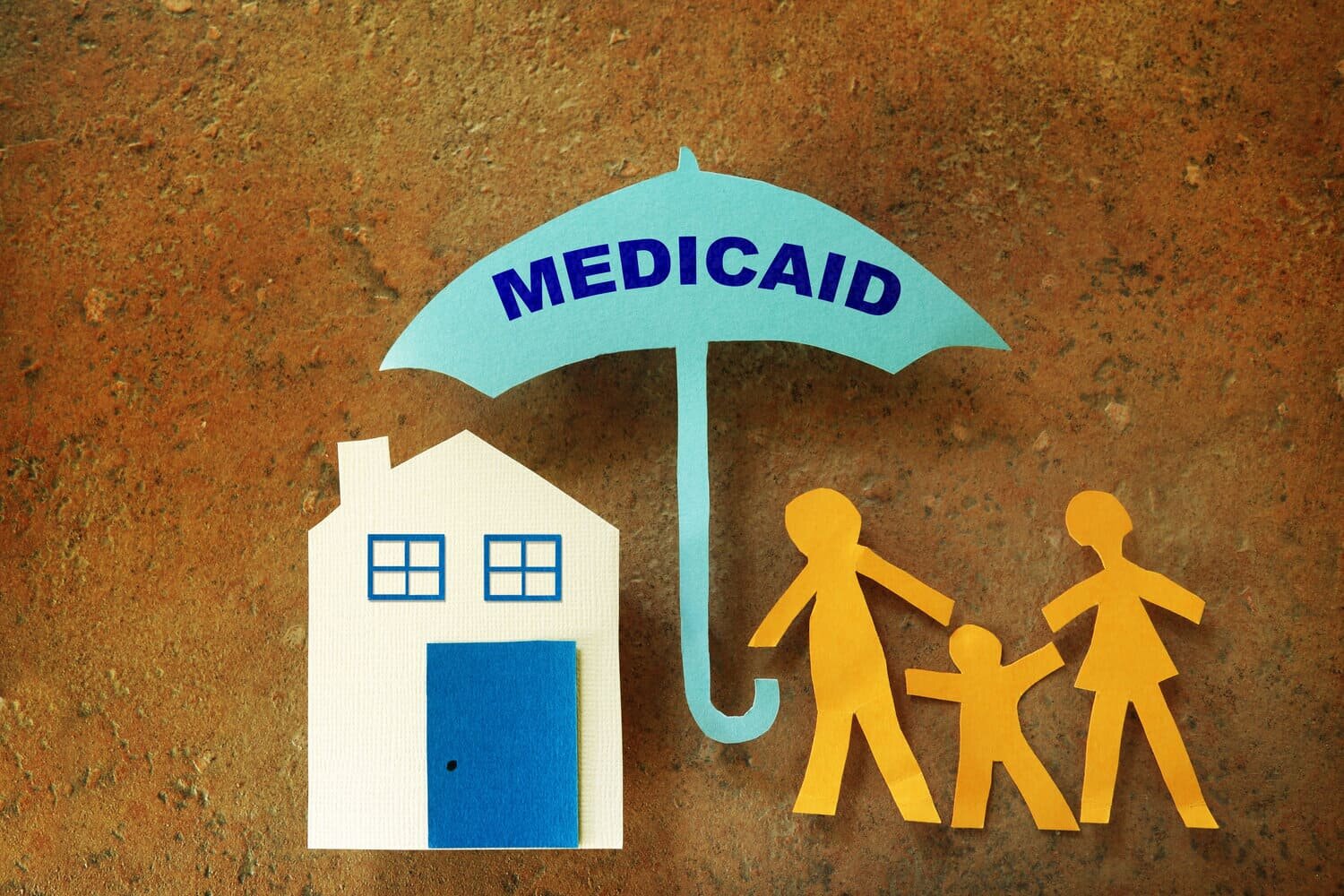 Obra de arte infantil de una casa de papel recortada junto a personas de pie bajo un paraguas que decía "Medicaid" en representación de Kansas Medicaid.