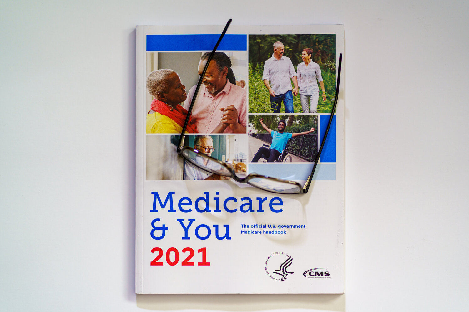 Fondo blanco con un par de gafas de lectura colocadas encima del manual 2021 Medicare and You.