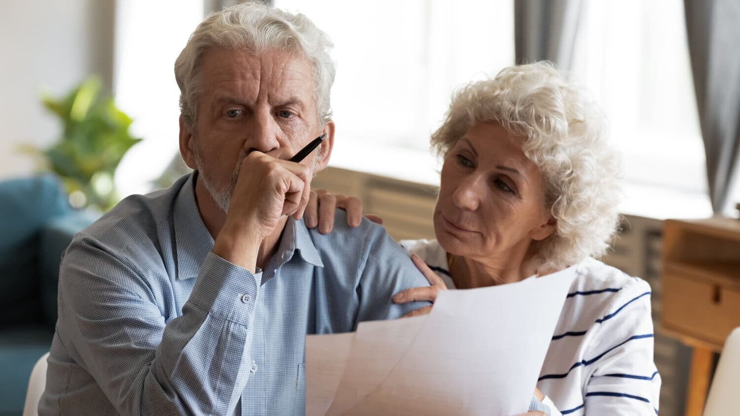 Una pareja de ancianos caucásicos miran atentamente los papeles de Medicare que tienen en sus manos e intentan decidir qué plan elegir.